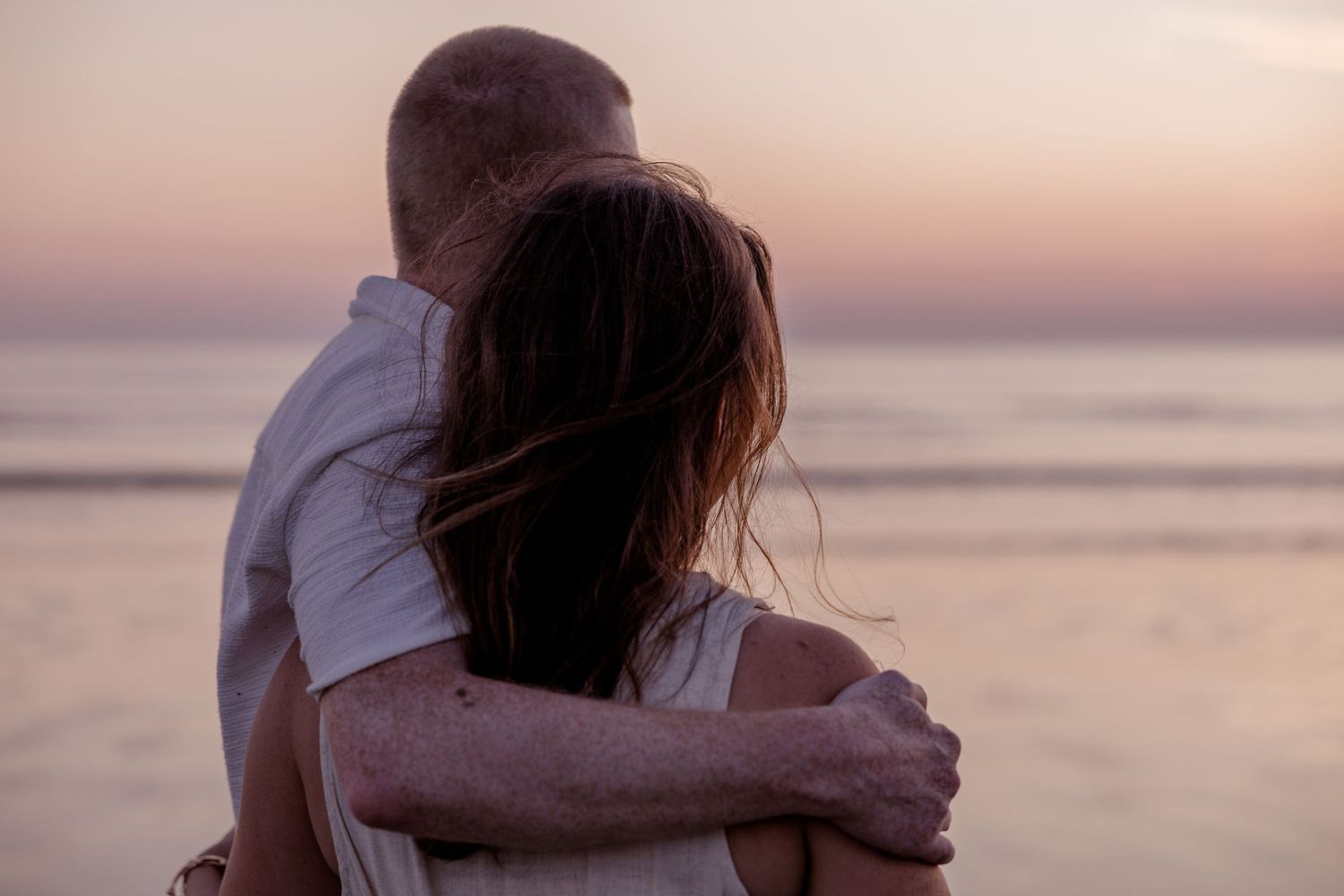 Couple embracing on a beach at sunset, sharing a romantic moment with ocean waves in the background.