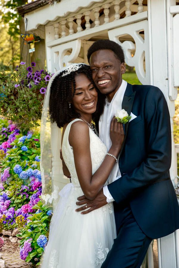 Bride and groom smiling together outdoors surrounded by flowers during wedding portrait