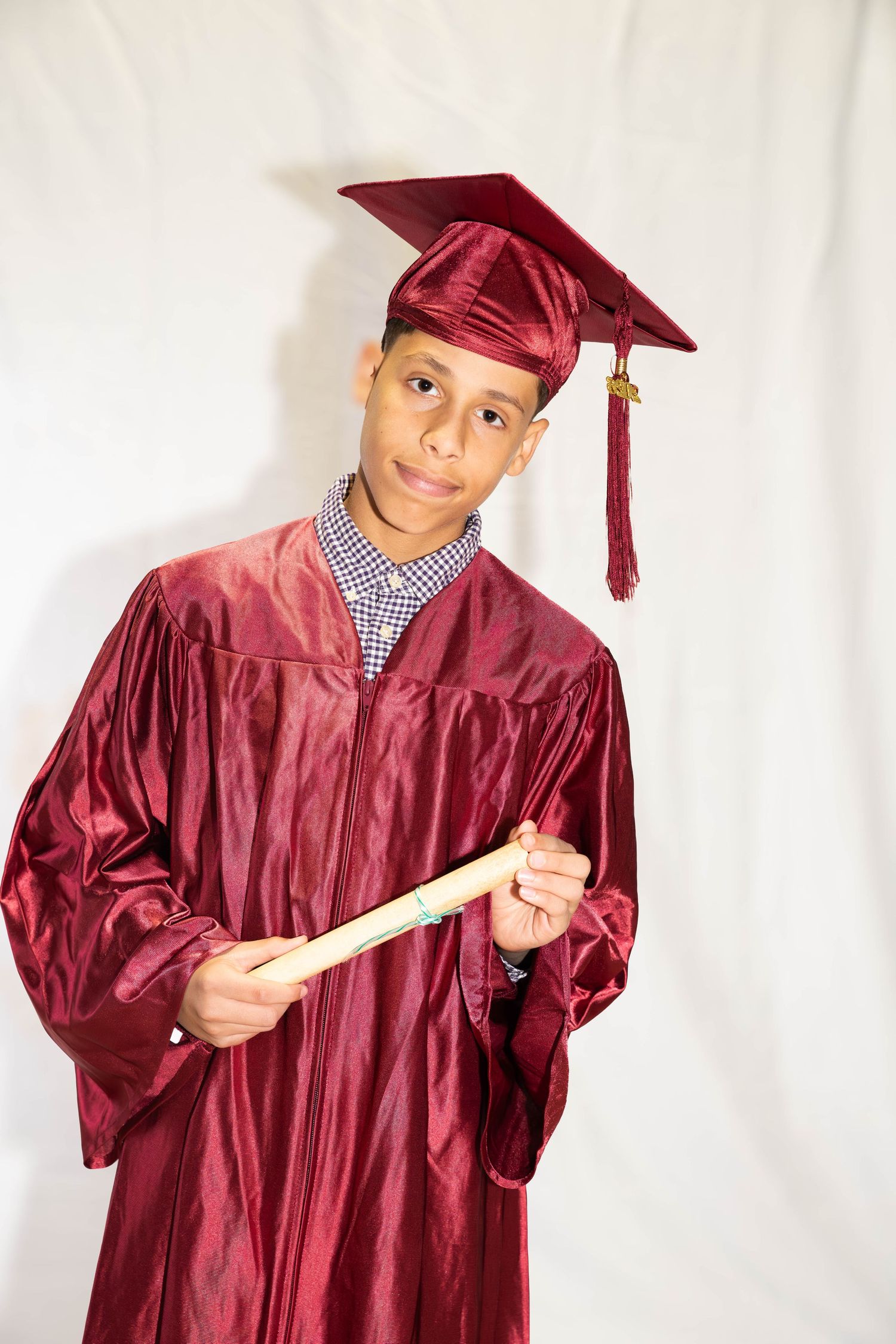 Graduate wearing a red cap and gown holding a diploma for a studio graduation portrait.