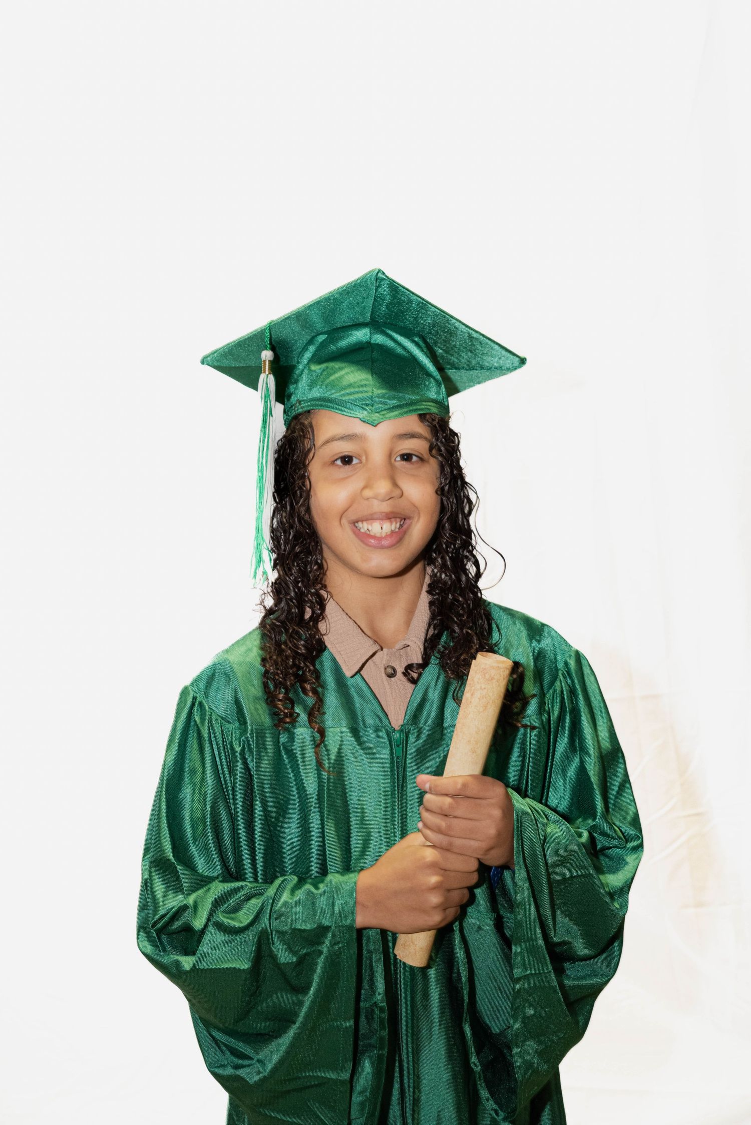 Child wearing a green graduation cap and gown for a school portrait session.