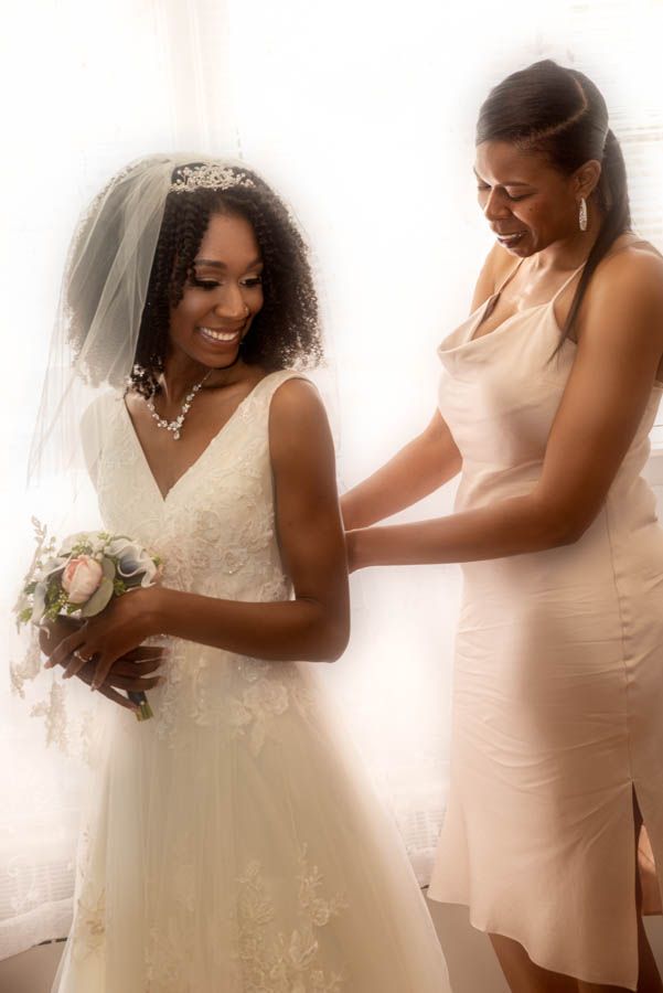 Bridesmaid helping bride with dress during wedding preparation