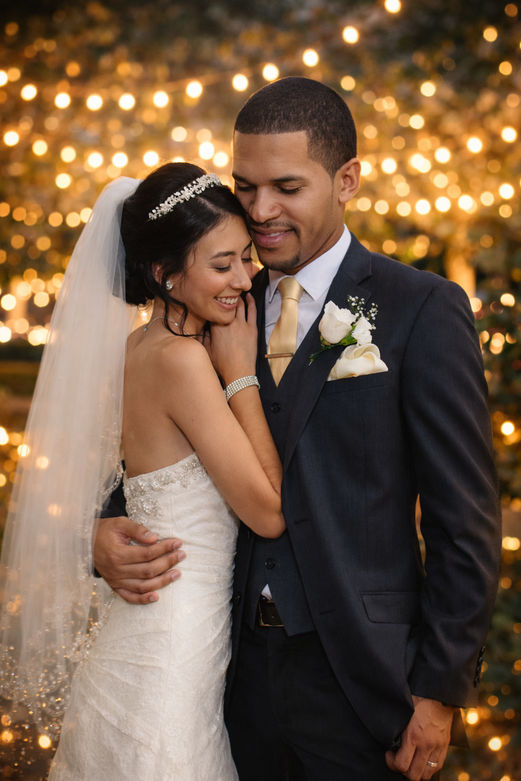 Romantic wedding portrait of a bride and groom embracing under warm golden string lights, with soft glowing bokeh and sparkler light creatin