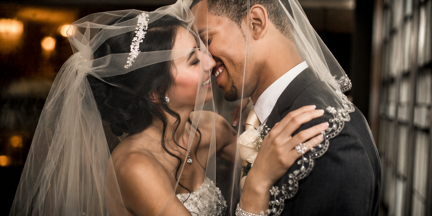 Close-up of bride and groom kissing under veil