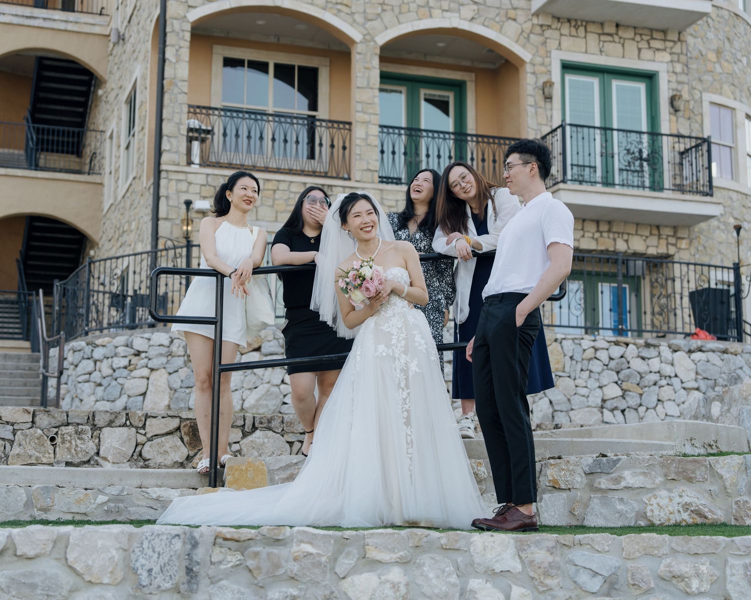 Bride posing with bridesmaids and guests on stone steps outside a beautiful wedding venue.