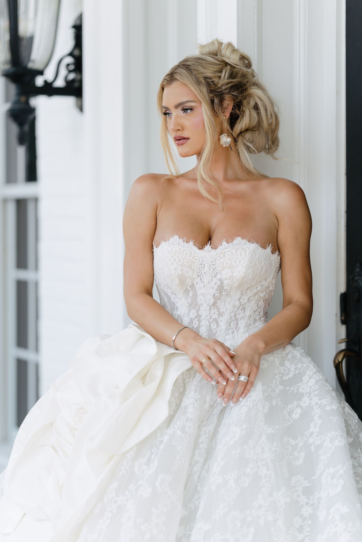 Beautiful blonde bride in strapless lace wedding gown poses gracefully against white columns.