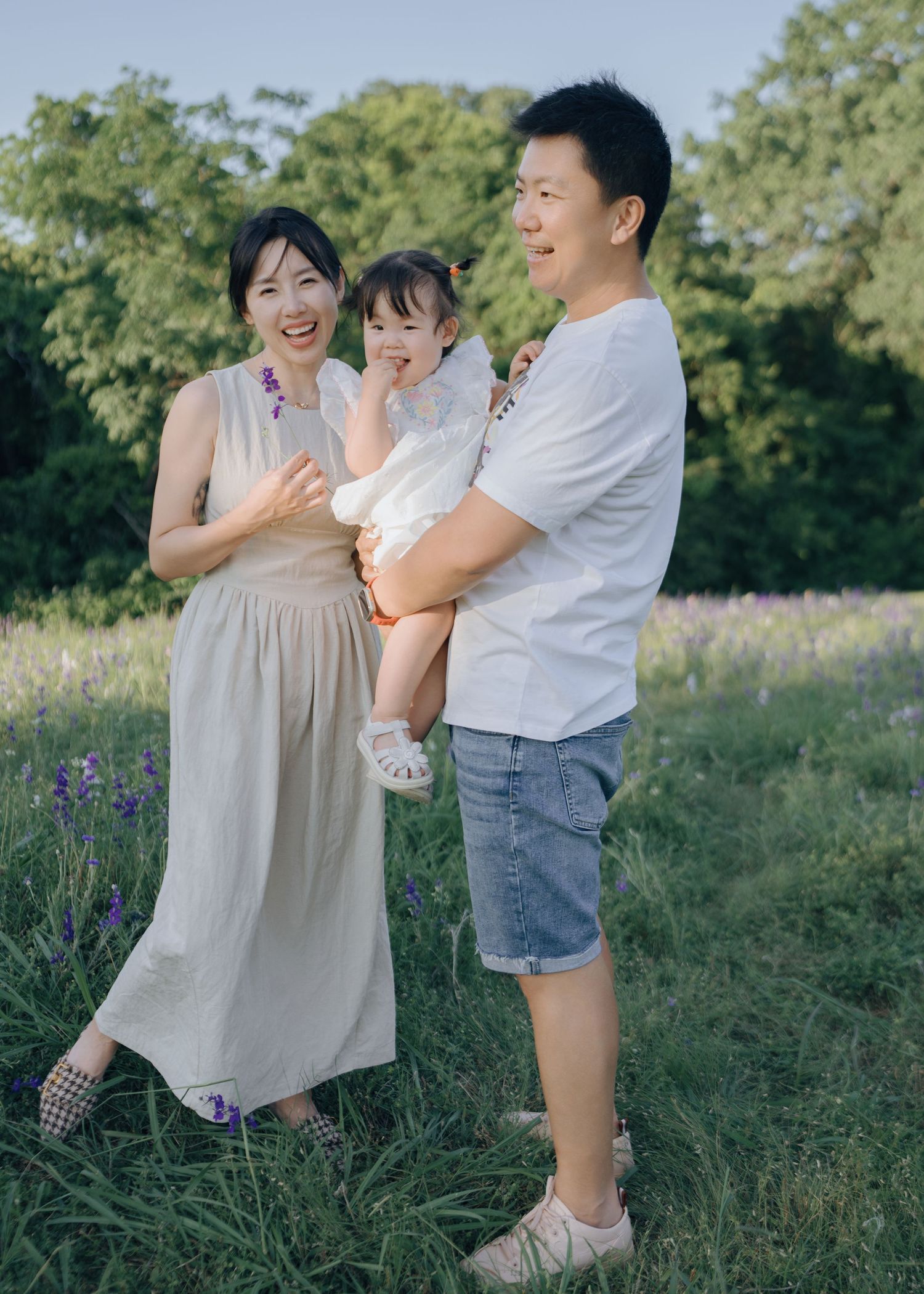 Happy Asian family with parents and toddler daughter posing in a purple wildflower meadow.