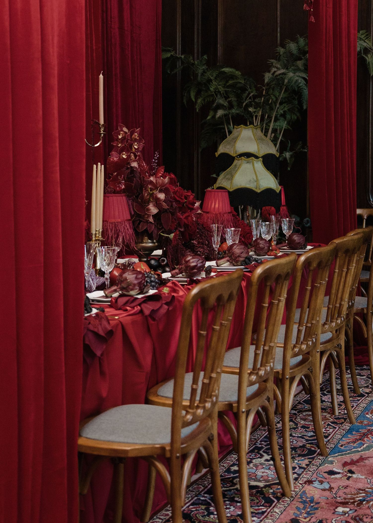 Luxurious red wedding reception table with gold chairs, candles, and dramatic crimson drapery.