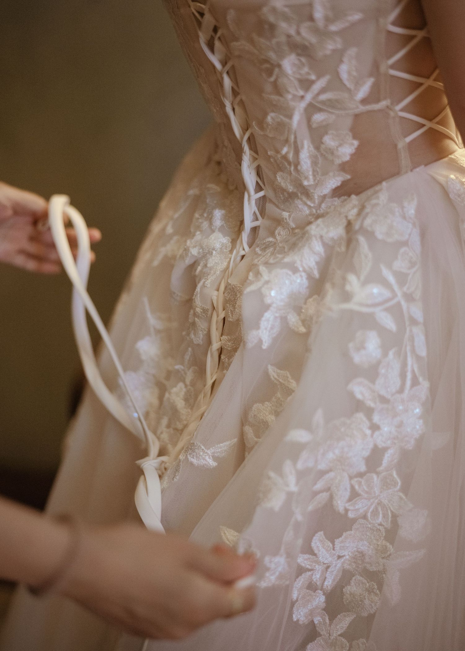 Close-up detail of a bride's corset lace-up wedding gown with delicate floral applique embroidery.