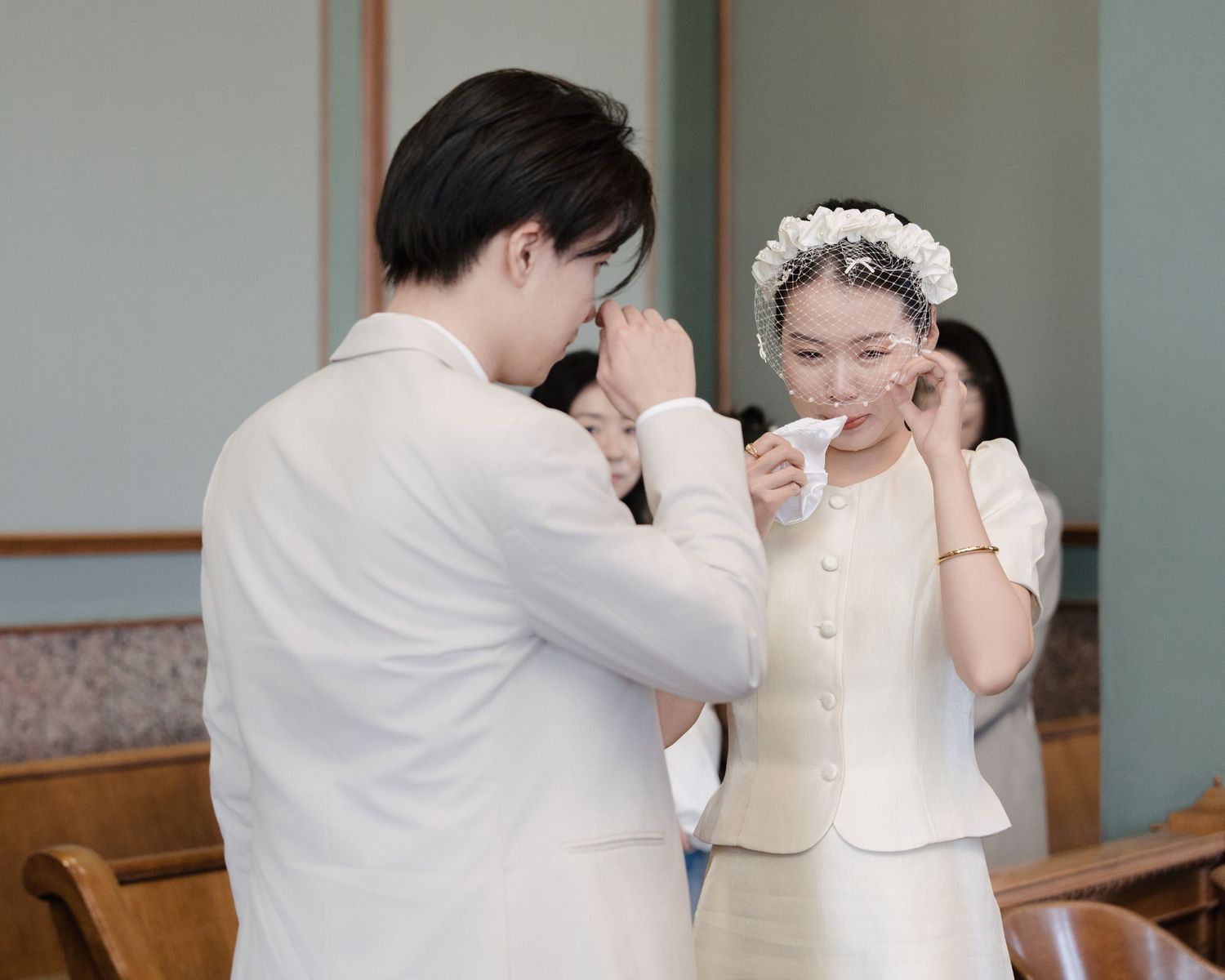 Emotional Asian couple crying during wedding ceremony in church, bride wearing floral headpiece.