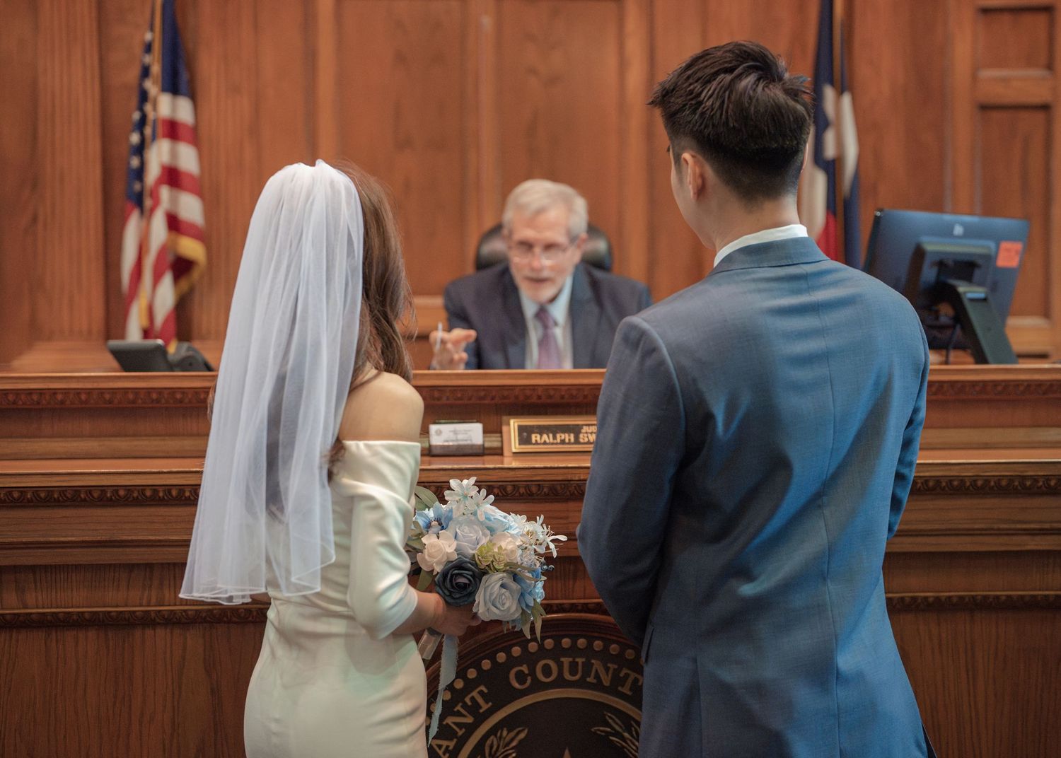 Couple exchanging vows before judge during intimate courthouse wedding ceremony.