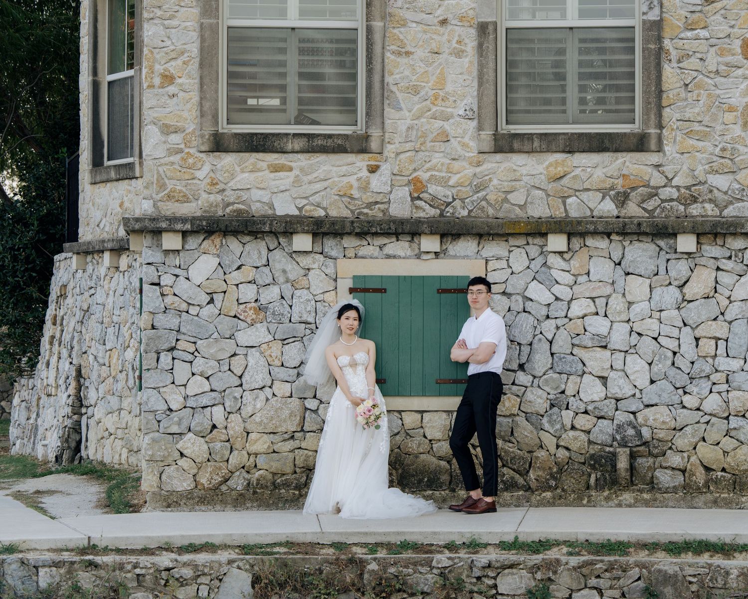 Bride and groom standing before a rustic stone building with a green door on their wedding day.