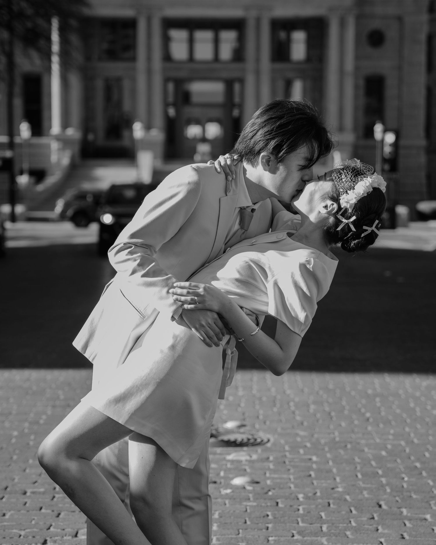 Black and white photo of groom dipping bride in a romantic kiss on cobblestone street.