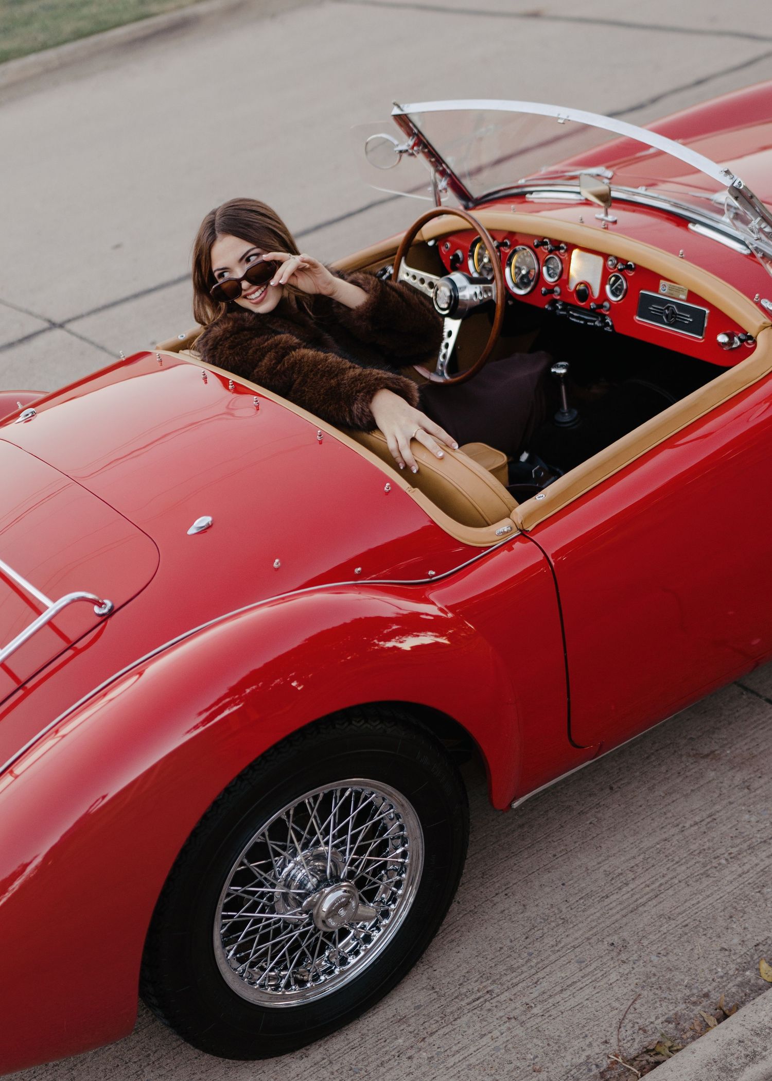 Aerial view of woman in fur coat sitting in classic red MGA convertible roadster.