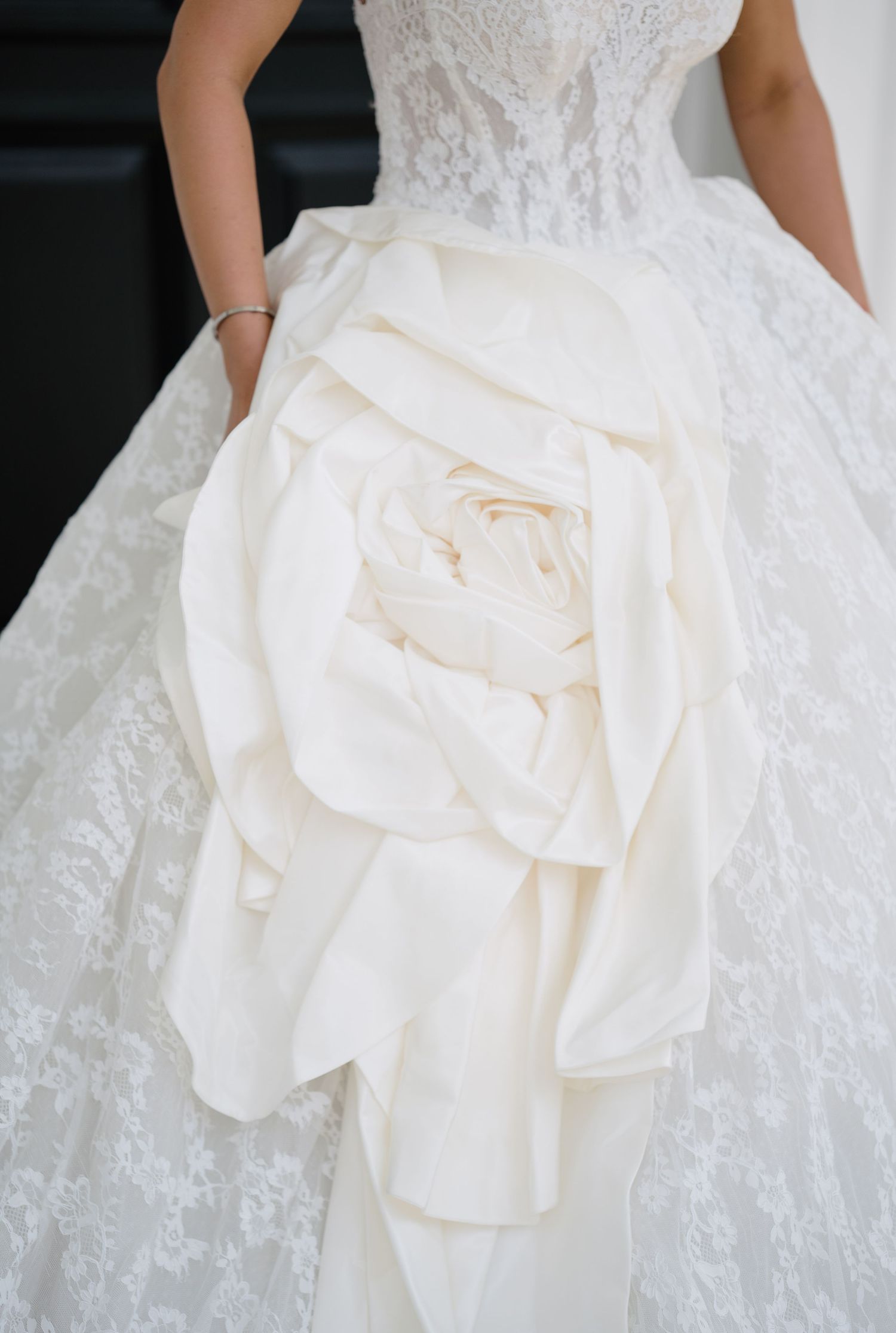 Elegant strapless lace wedding gown featuring a dramatic oversized white rose detail on the full ball skirt.