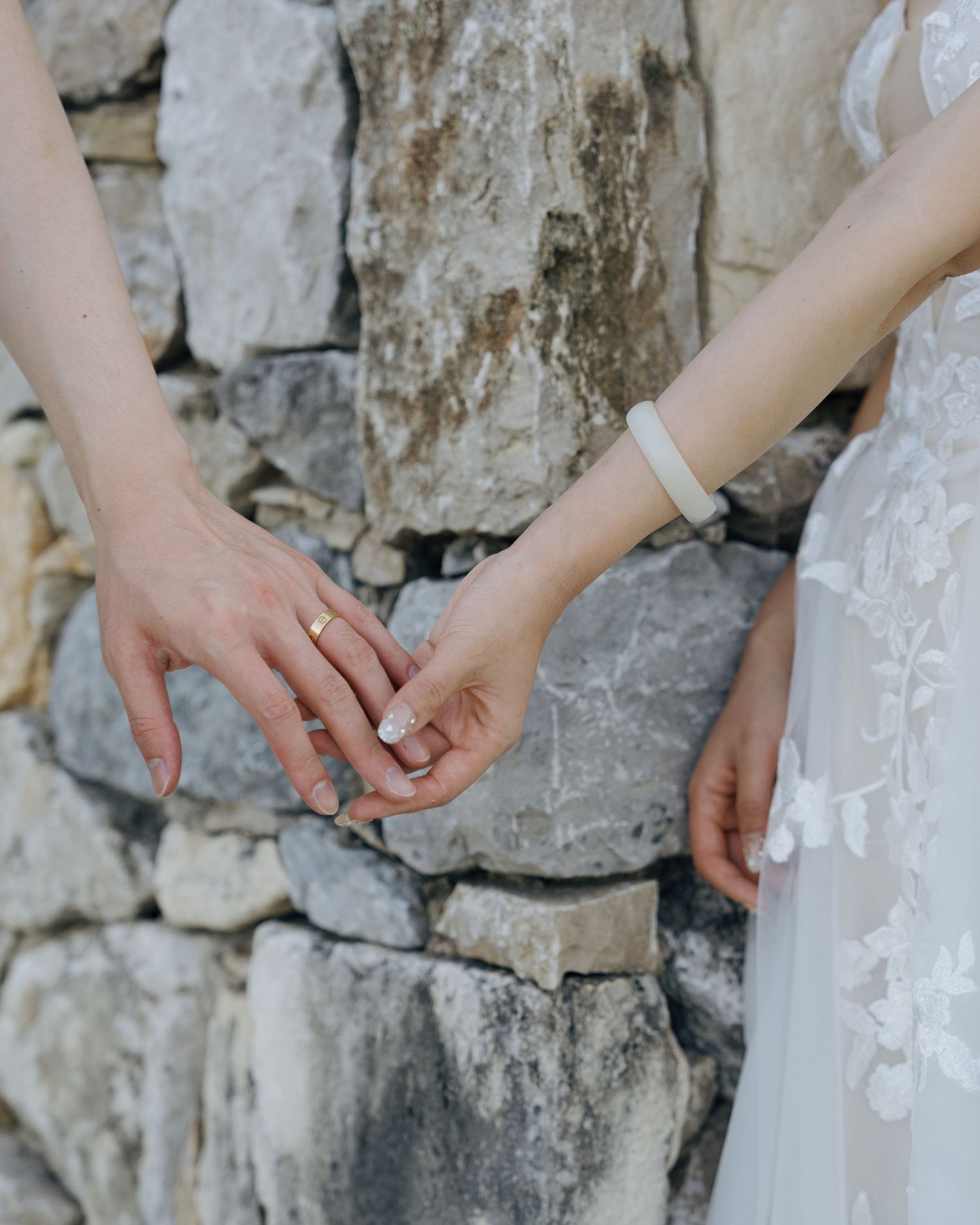 Close-up of bride and groom exchanging rings at a rustic stone wall wedding ceremony.