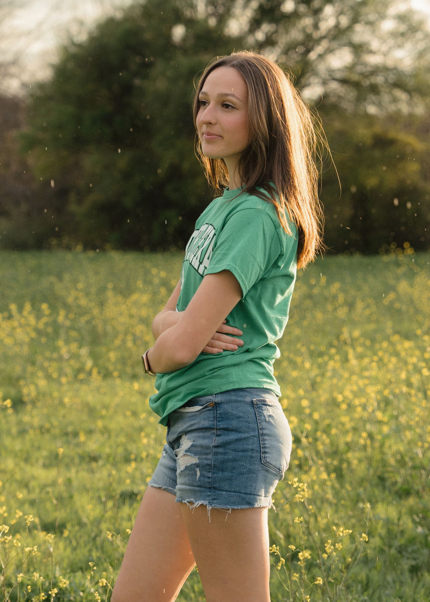 Young woman in green North Texas tee and denim shorts posing in a yellow wildflower field.