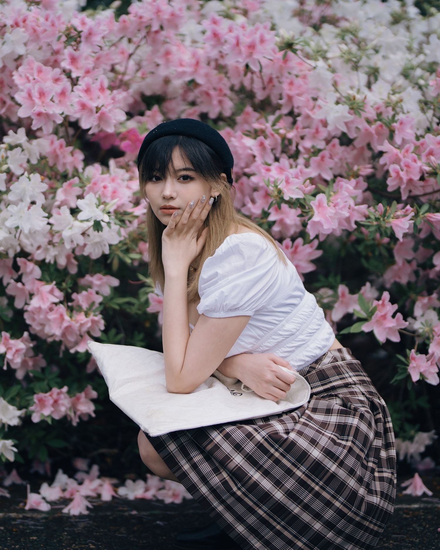 Young woman in plaid skirt and white top poses among pink and white azalea blooms.