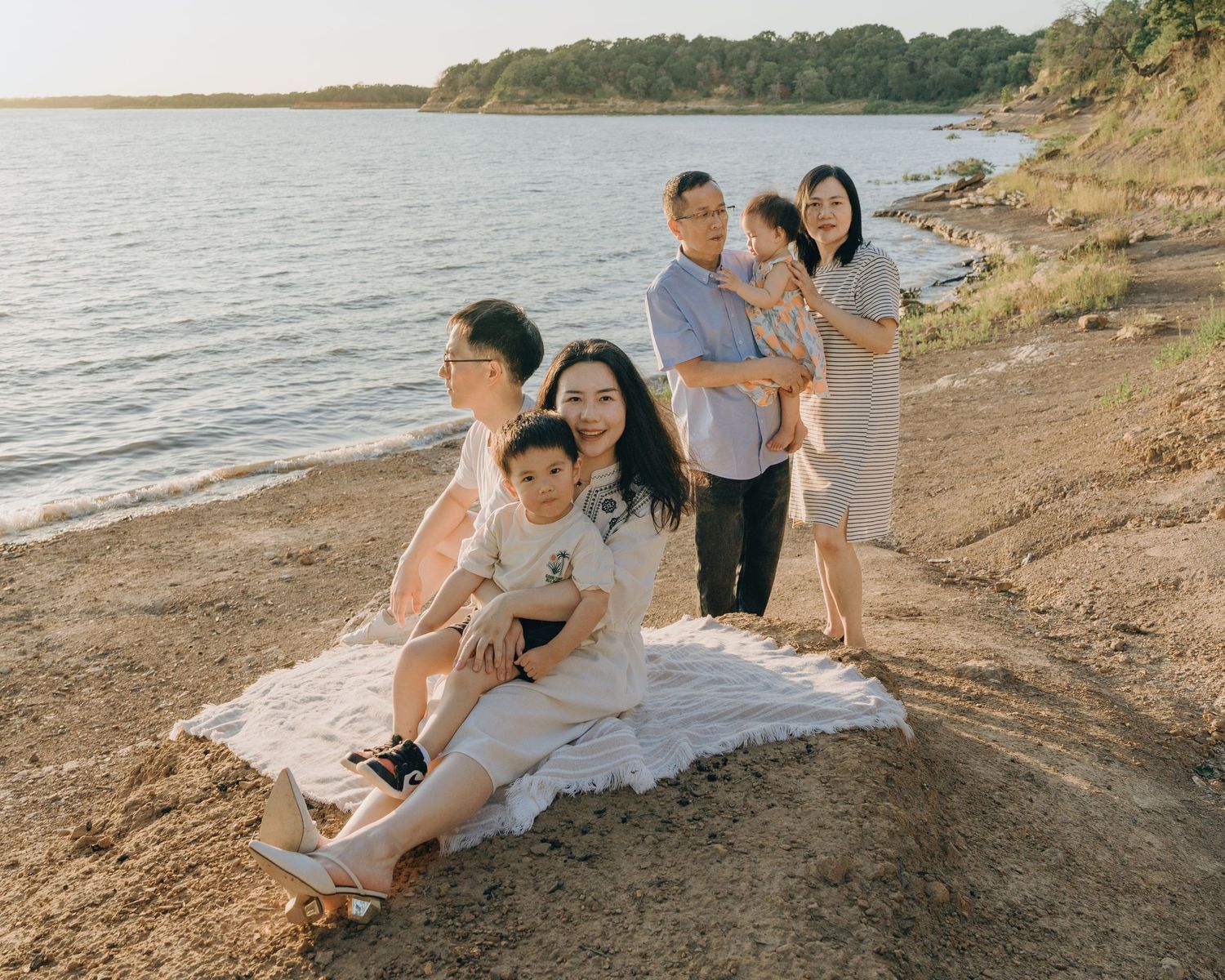 Asian family of six posing on a sandy beach shore at golden hour with calm water in the background.