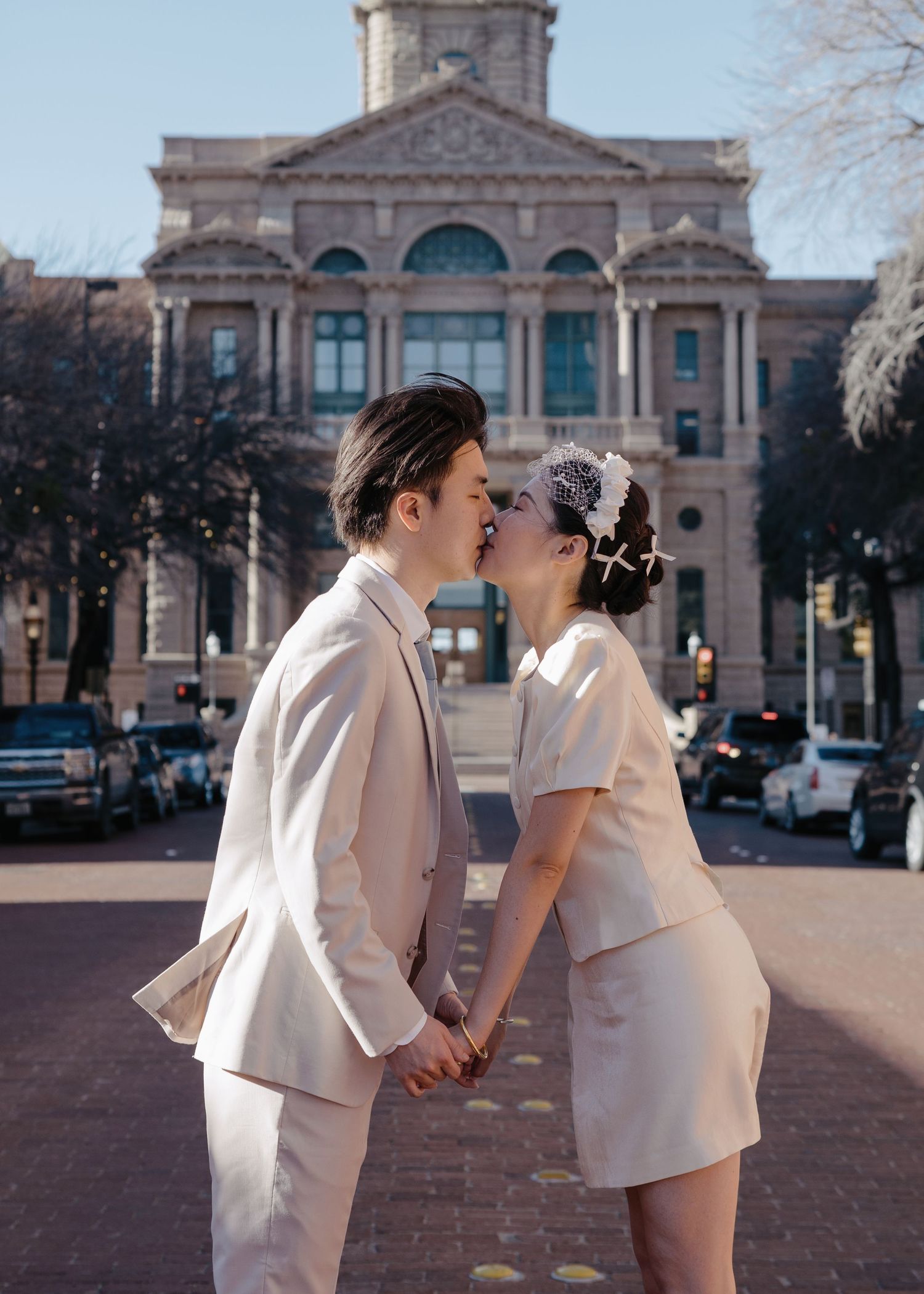 Bride and groom kissing while holding hands in front of a historic stone courthouse building.