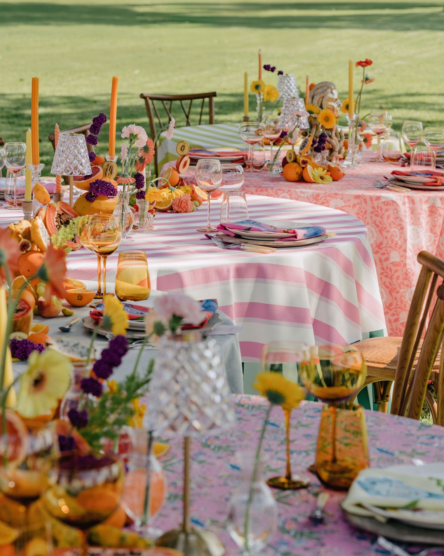 Colorful outdoor wedding reception tables with pink striped linens, candles, and vibrant floral arrangements.