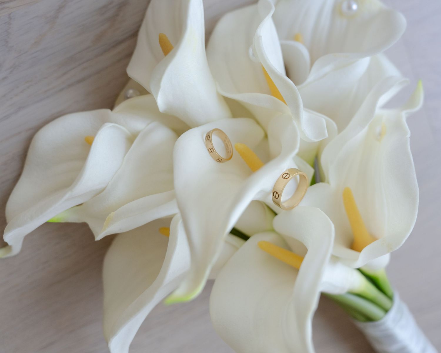 White calla lily bridal bouquet with two gold wedding rings nestled among the blooms.