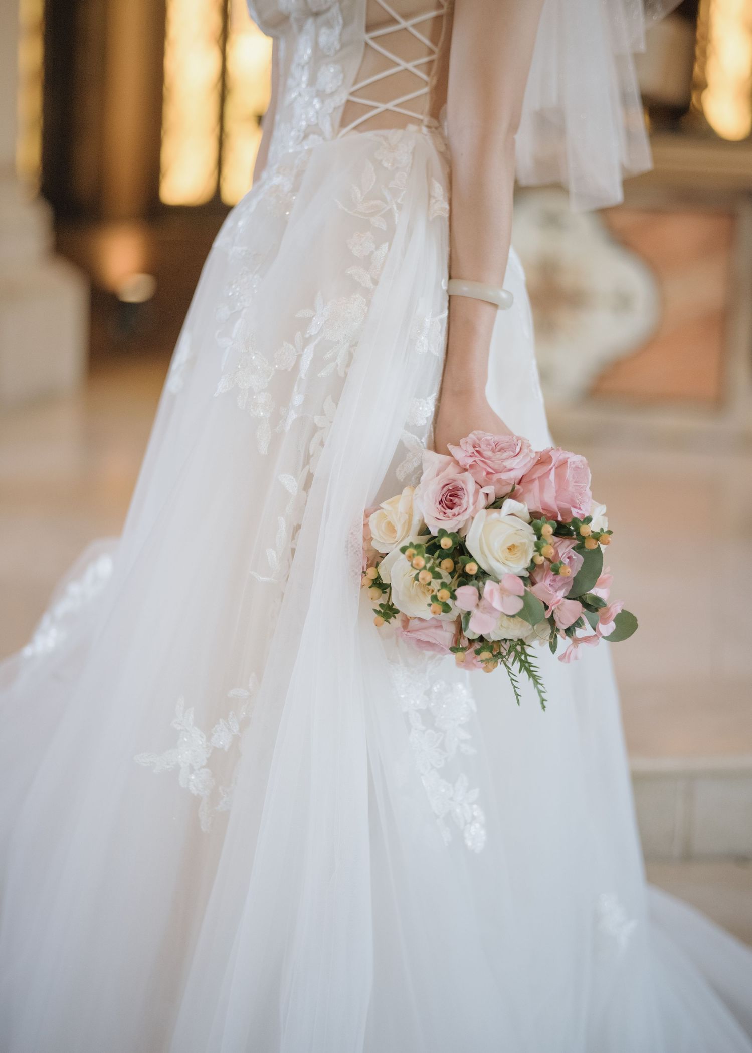 Bride in lace corset wedding gown holding pink and white rose bouquet with flowing tulle skirt.