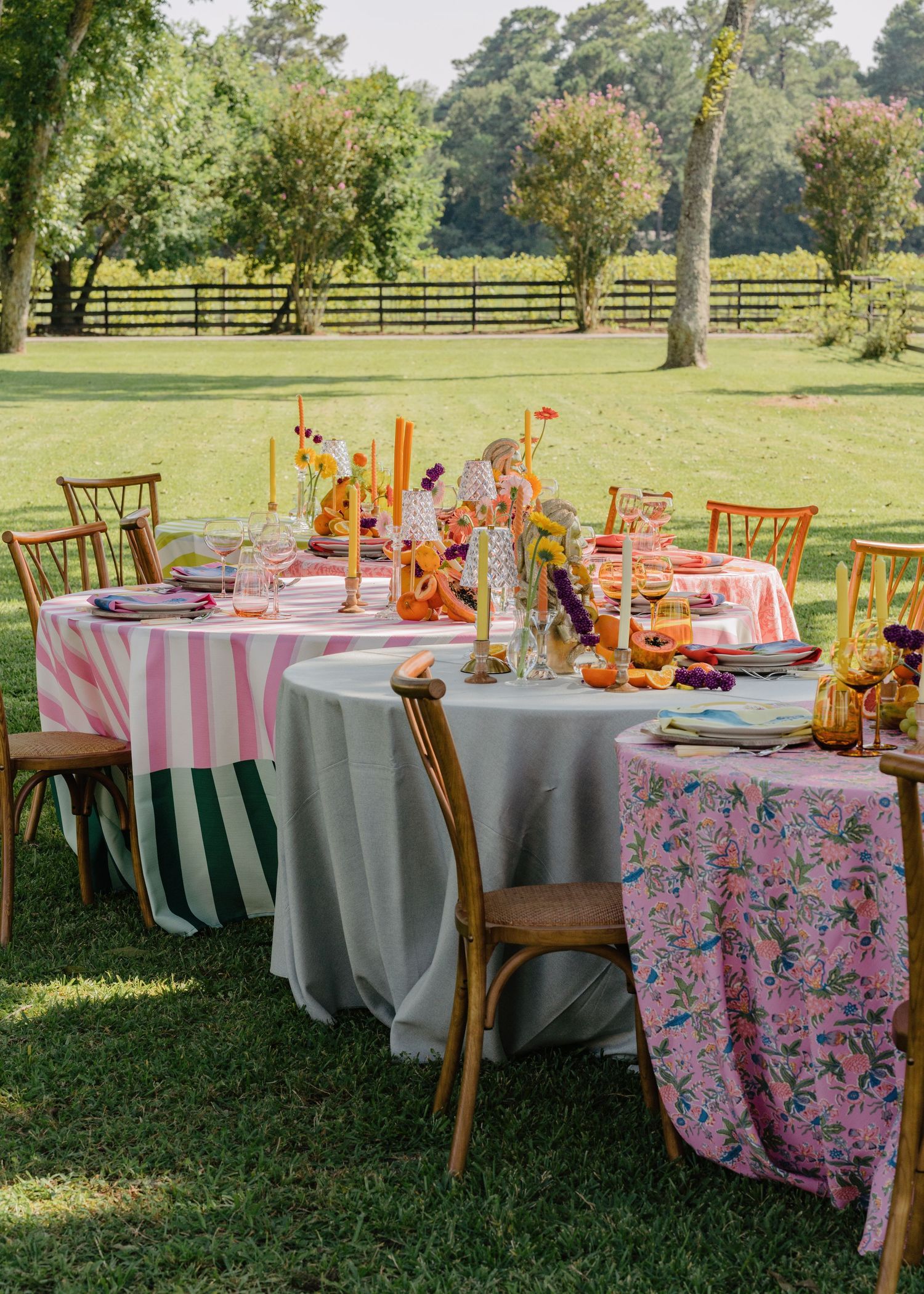 Colorful outdoor wedding reception tables with striped linens, floral centerpieces, and wooden chairs on green lawn.