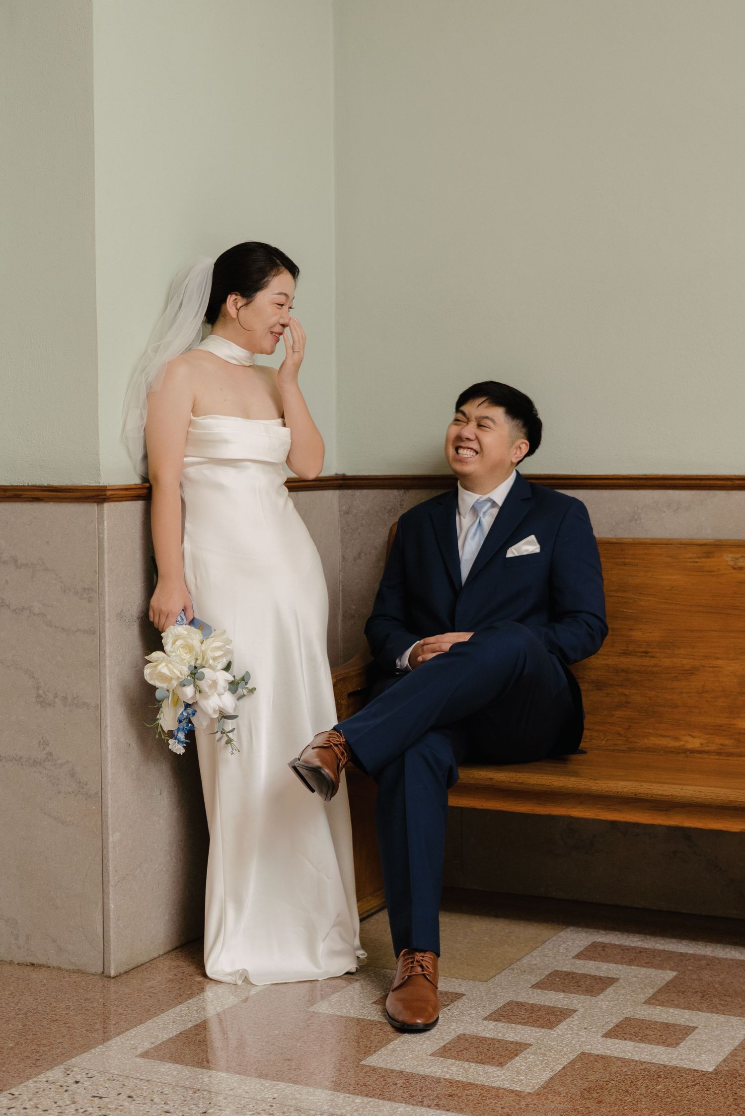 Bride in white satin gown and groom in navy suit share a joyful moment at a courthouse wedding.
