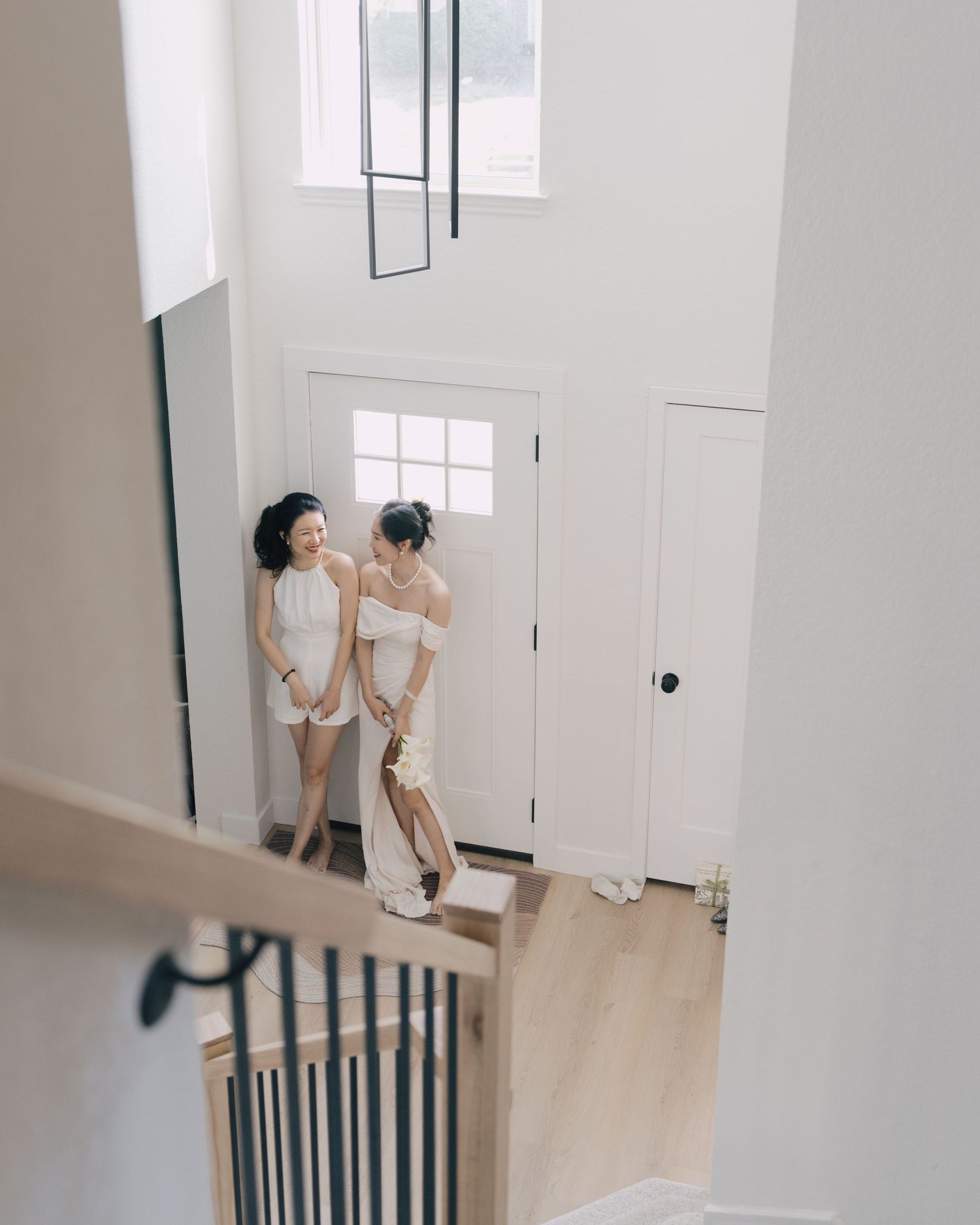 Aerial view of bride in white gown and bridesmaid chatting in bright modern foyer.
