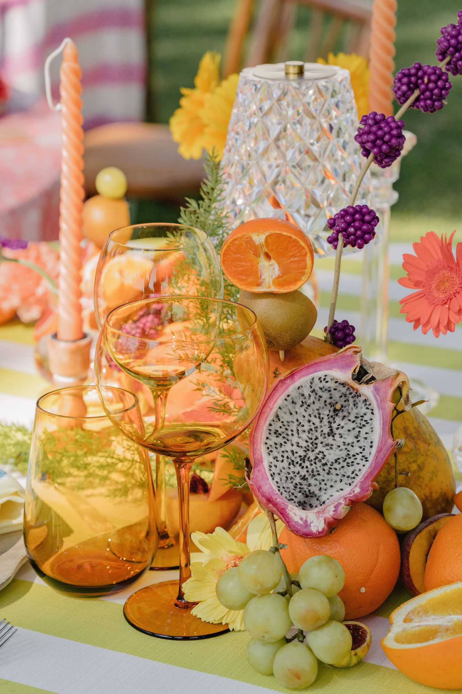 Vibrant wedding tablescape with amber glassware, dragon fruit, grapes, and colorful floral centerpiece.