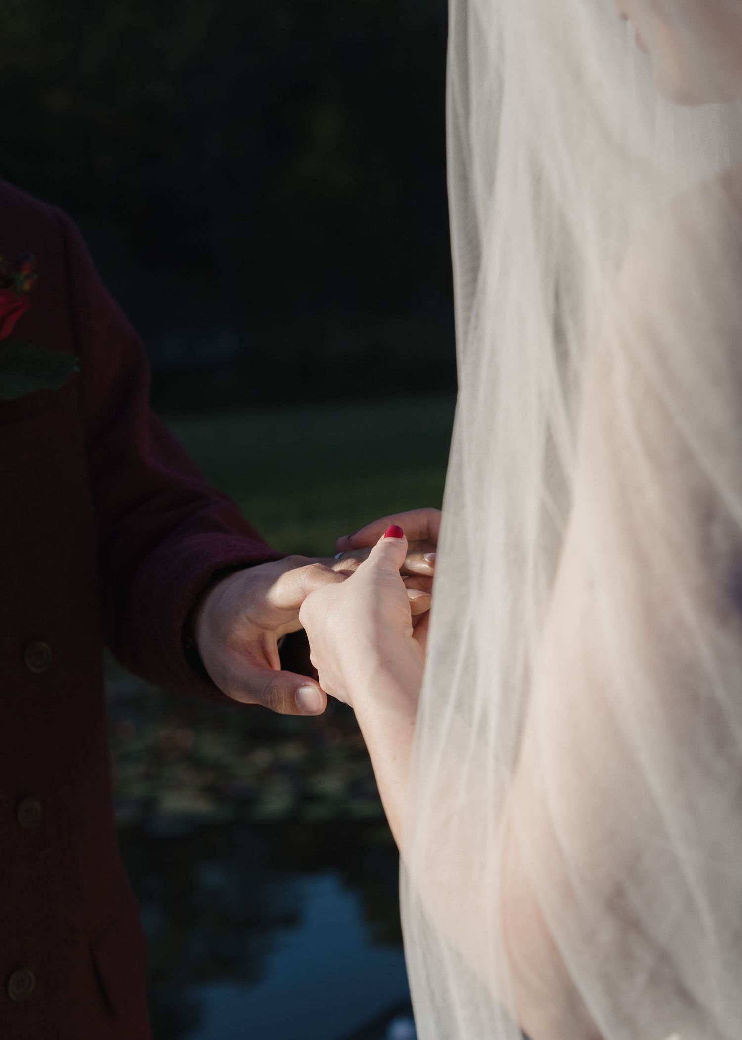 Close-up of bride and groom holding hands, her veil draped softly beside them outdoors.