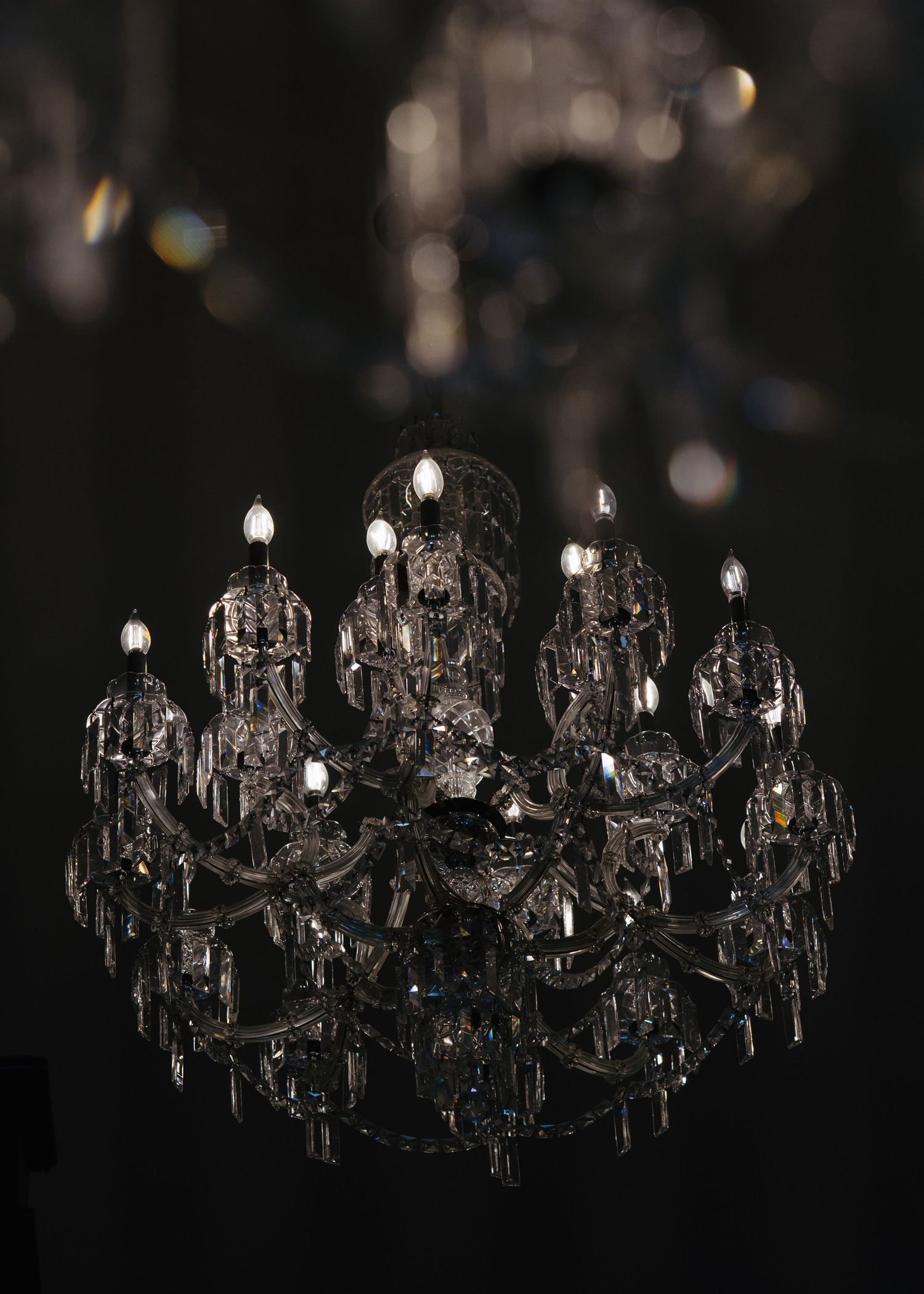 Dramatic crystal chandelier with candle lights glowing against dark ceiling at wedding venue.