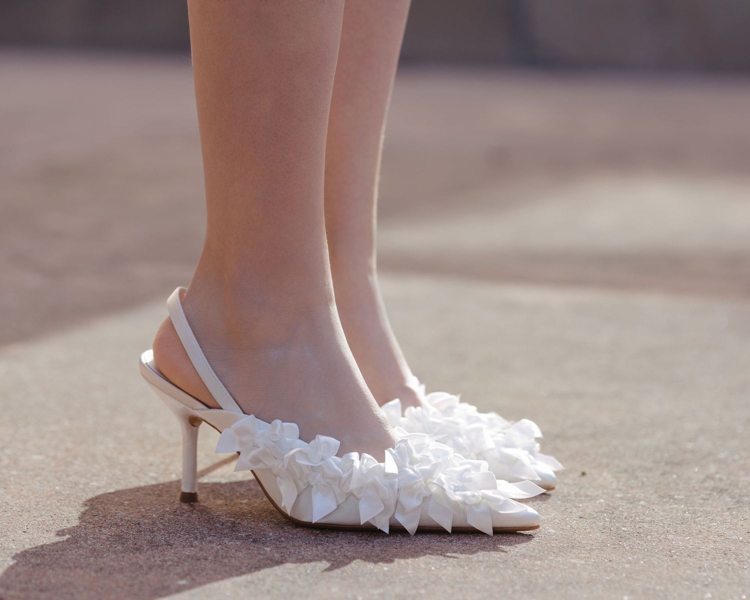 Close-up of elegant white ruffled slingback heels worn by a bride on her wedding day.