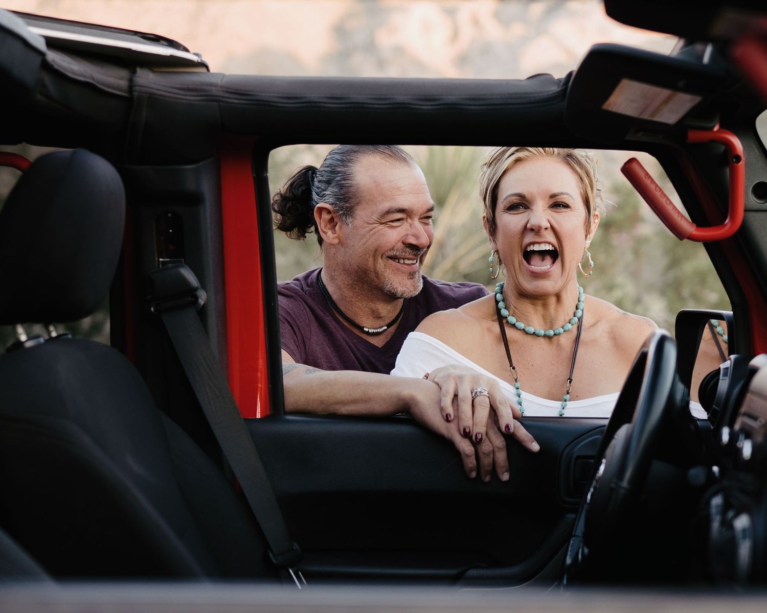 Laughing couple enjoying a joyful moment together inside a red convertible Jeep outdoors.