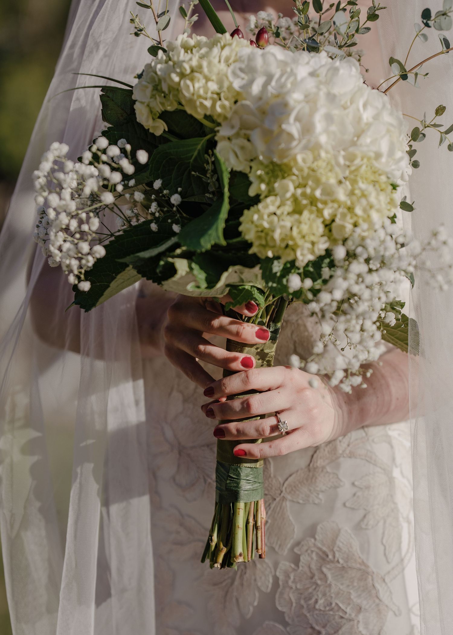 Bride holding white hydrangea and baby's breath wedding bouquet with red manicured nails.