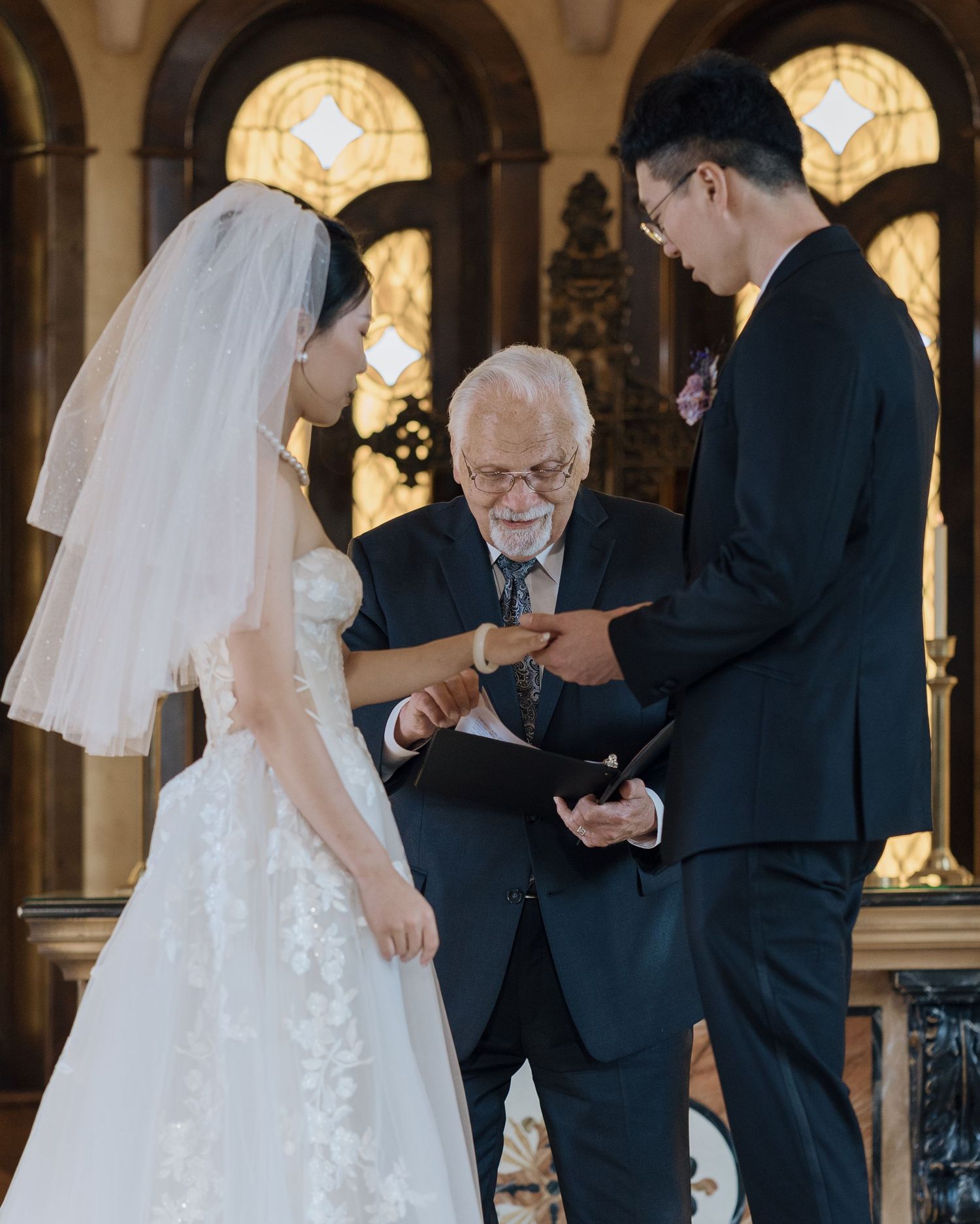 Bride and groom exchanging vows with an officiant inside an elegant church ceremony.