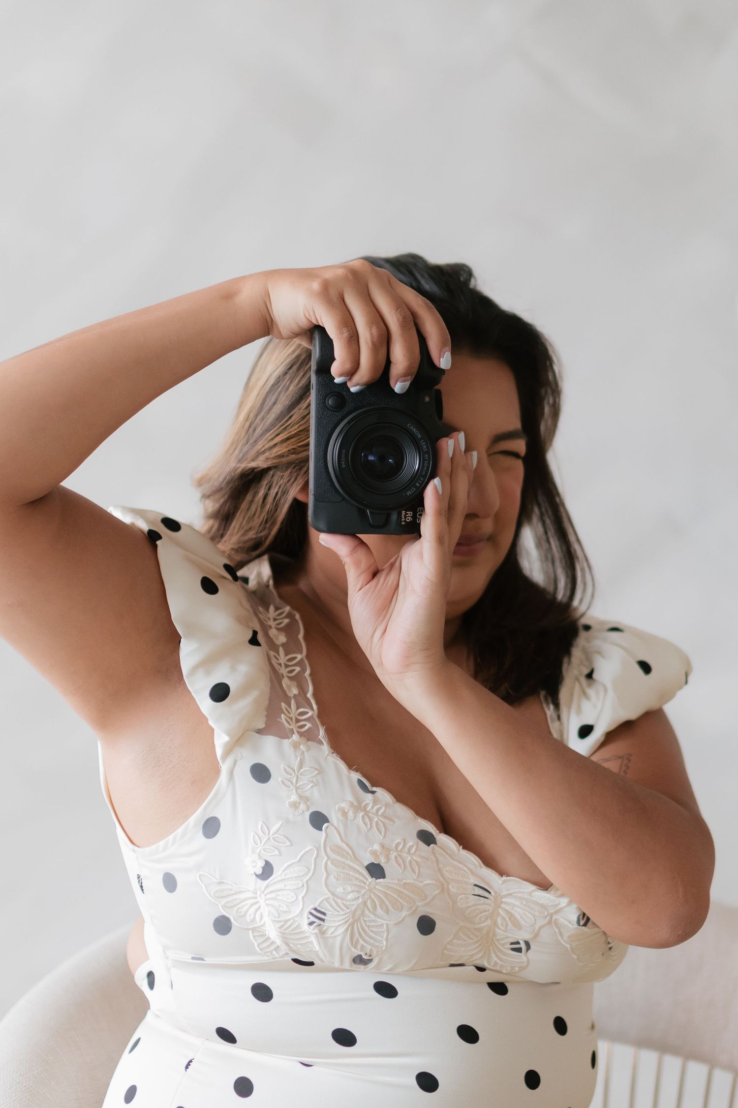 Female photographer in white polka dot dress taking photo with camera raised to eye.
