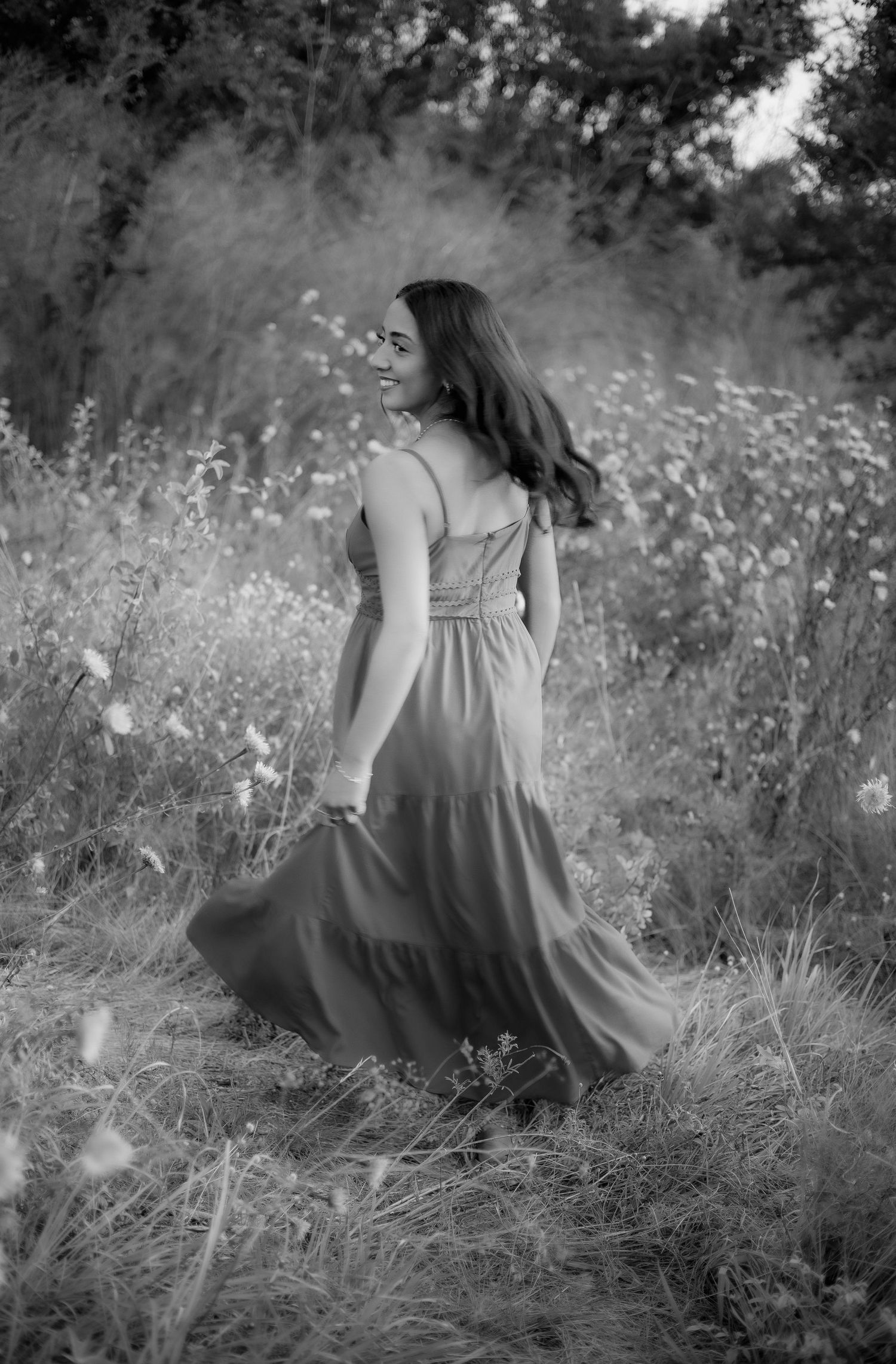 Young woman in flowing dress walking through a wildflower meadow in black and white photo.
