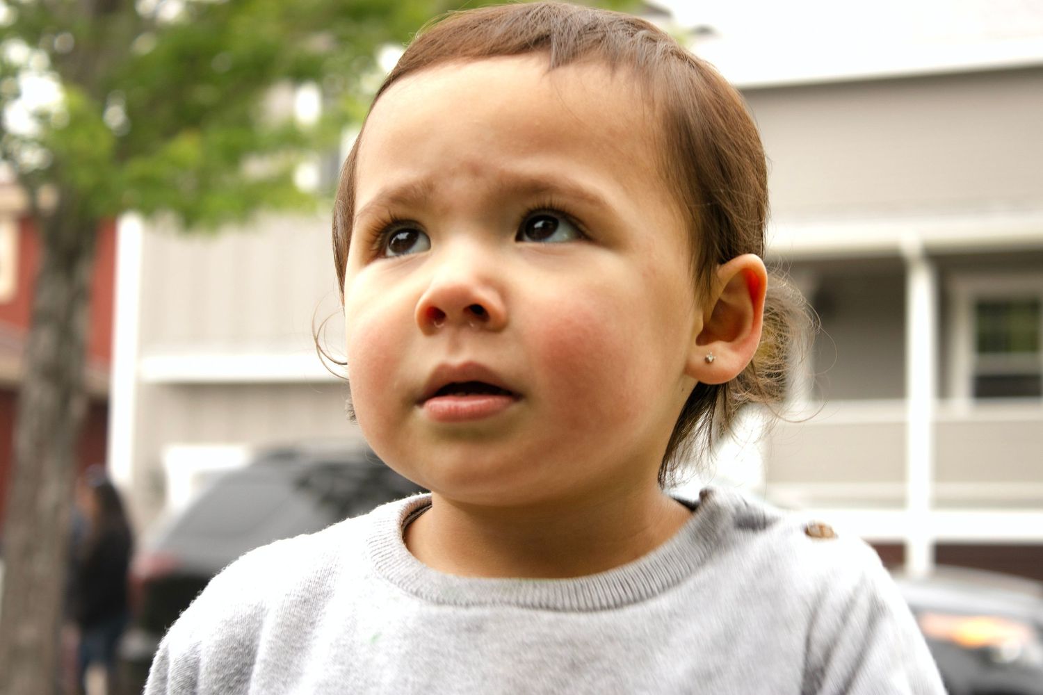 Close-up portrait of curious toddler boy with brown eyes looking upward outdoors.