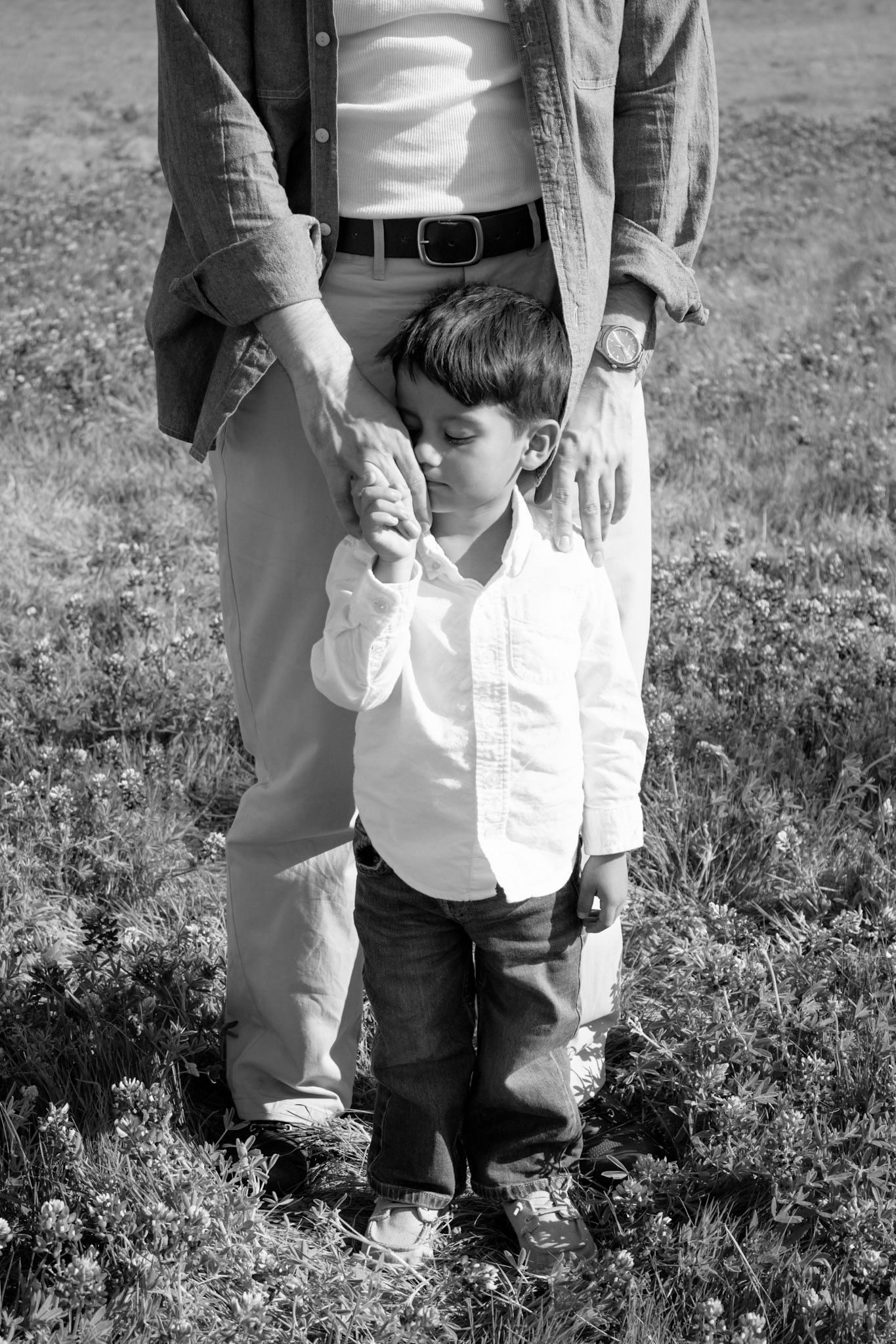 Black and white photo of a young child holding an adult's hand while standing in a grassy field outdoors.
