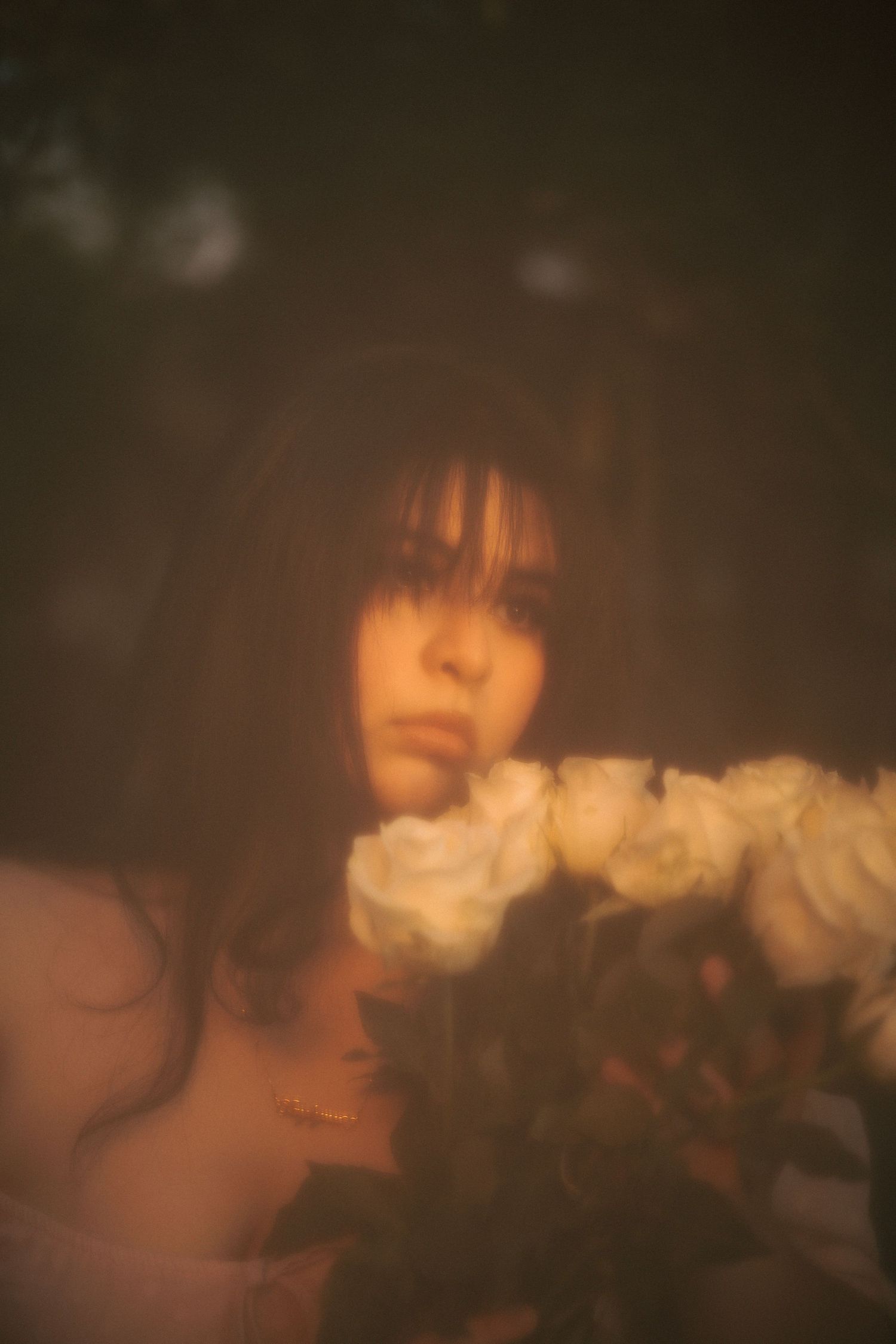 Dreamy soft-focus portrait of young woman gazing over bouquet of white roses in warm light.