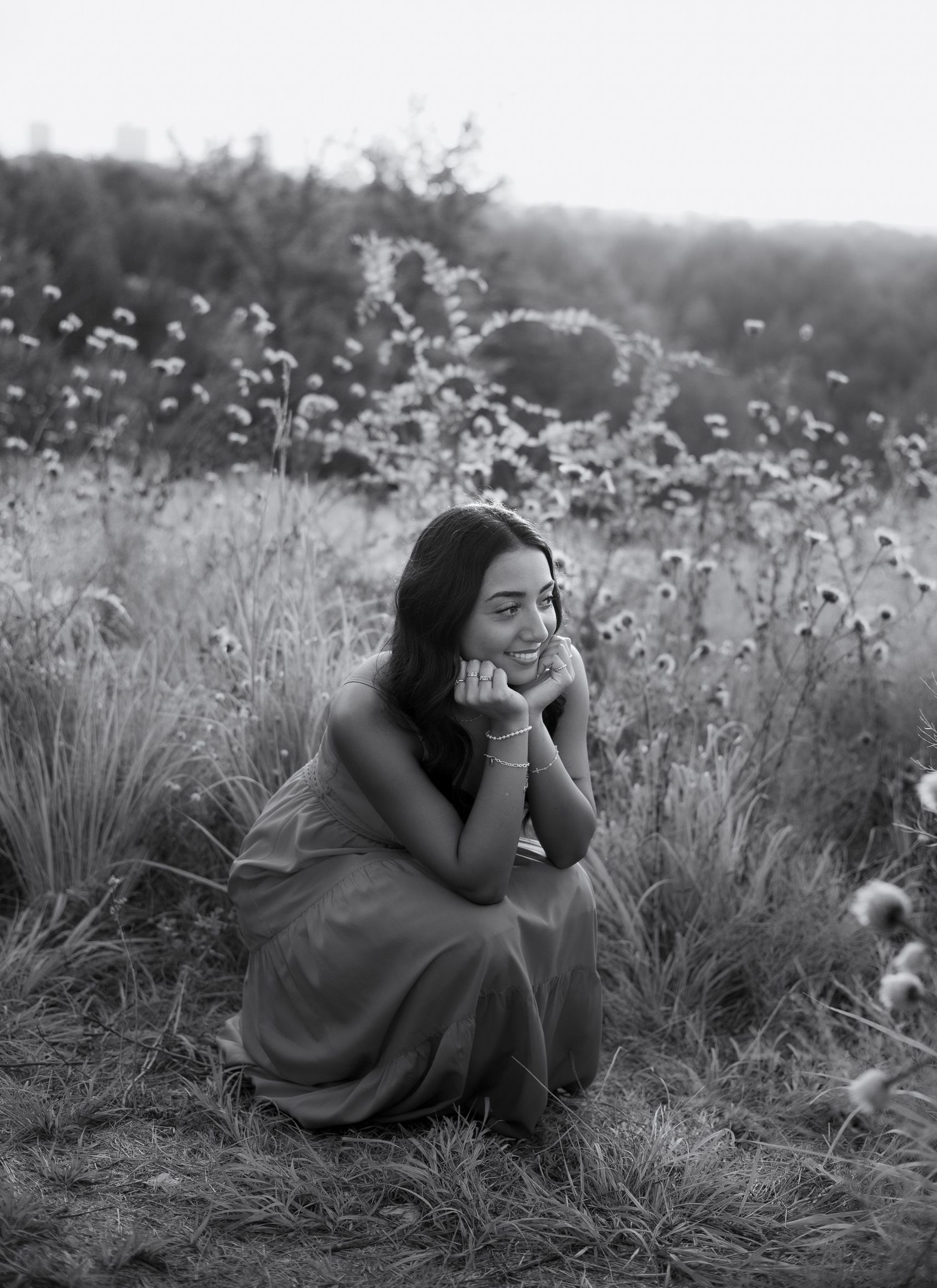 Black and white portrait of a young woman sitting in a wildflower field smiling softly.