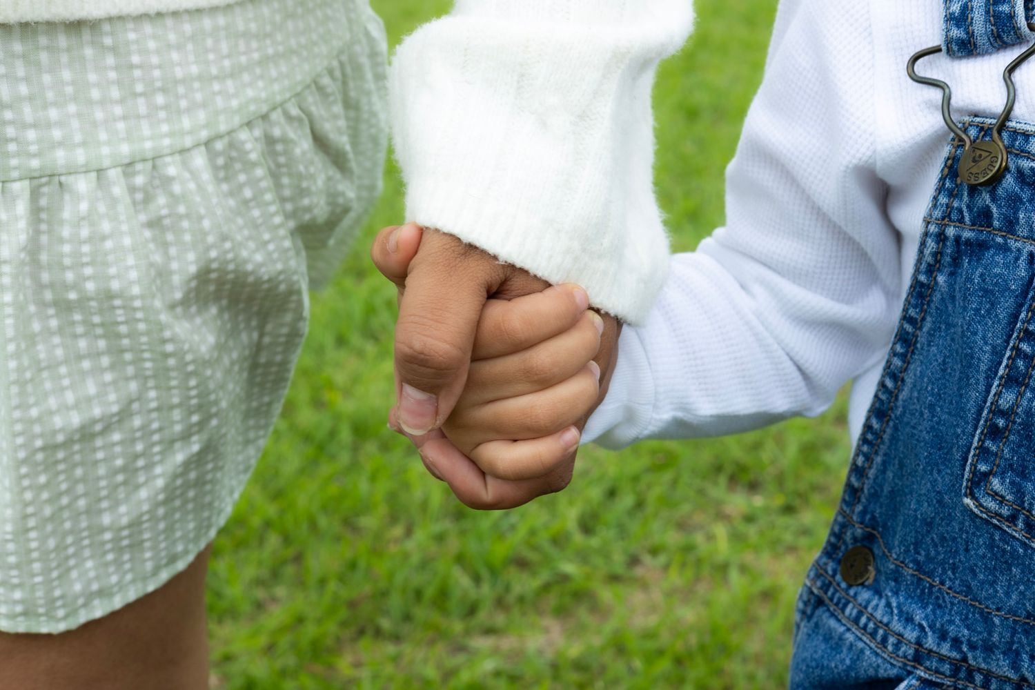 Two children holding hands outdoors on green grass, showing friendship and connection.