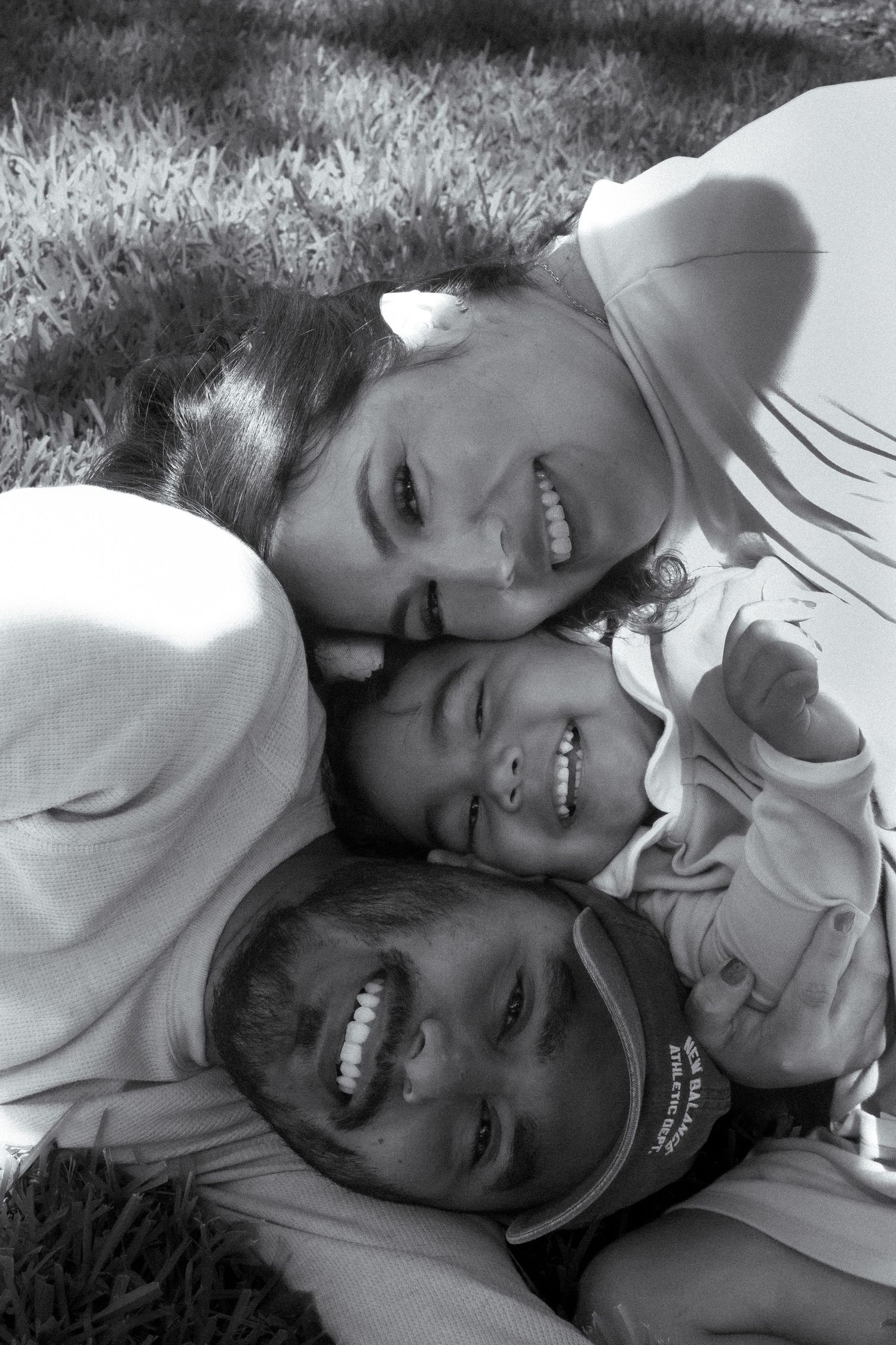 Black and white photo of a smiling family of three lying together on grass outdoors.