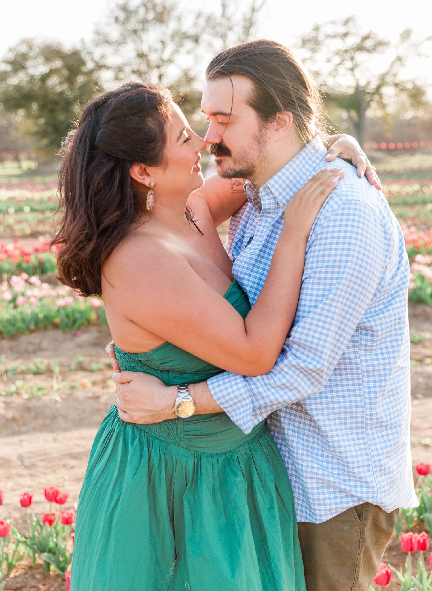Couple embracing and smiling in a colorful tulip field at golden hour.
