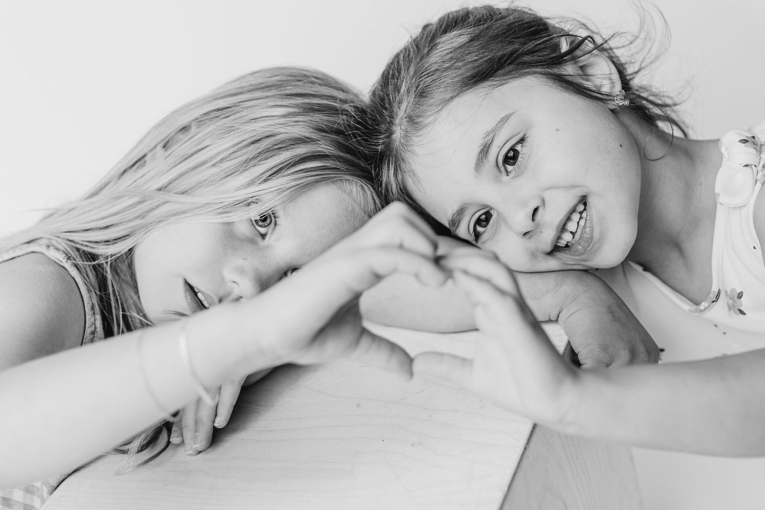 Two young girls leaning heads together making a heart shape with their hands in a black and white photo.