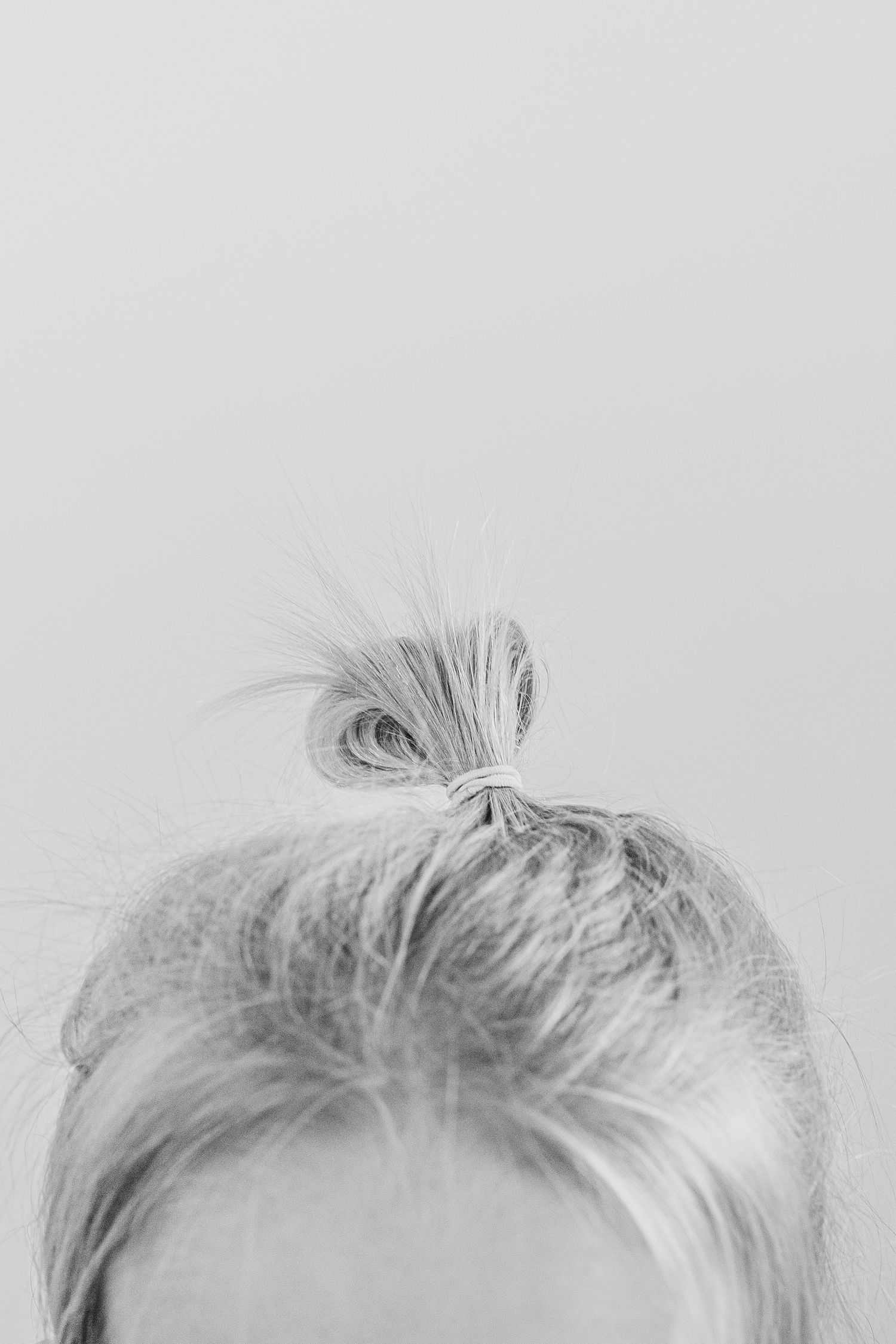 Black and white photo of a woman with blonde hair styled in a messy top knot bun against a light background.