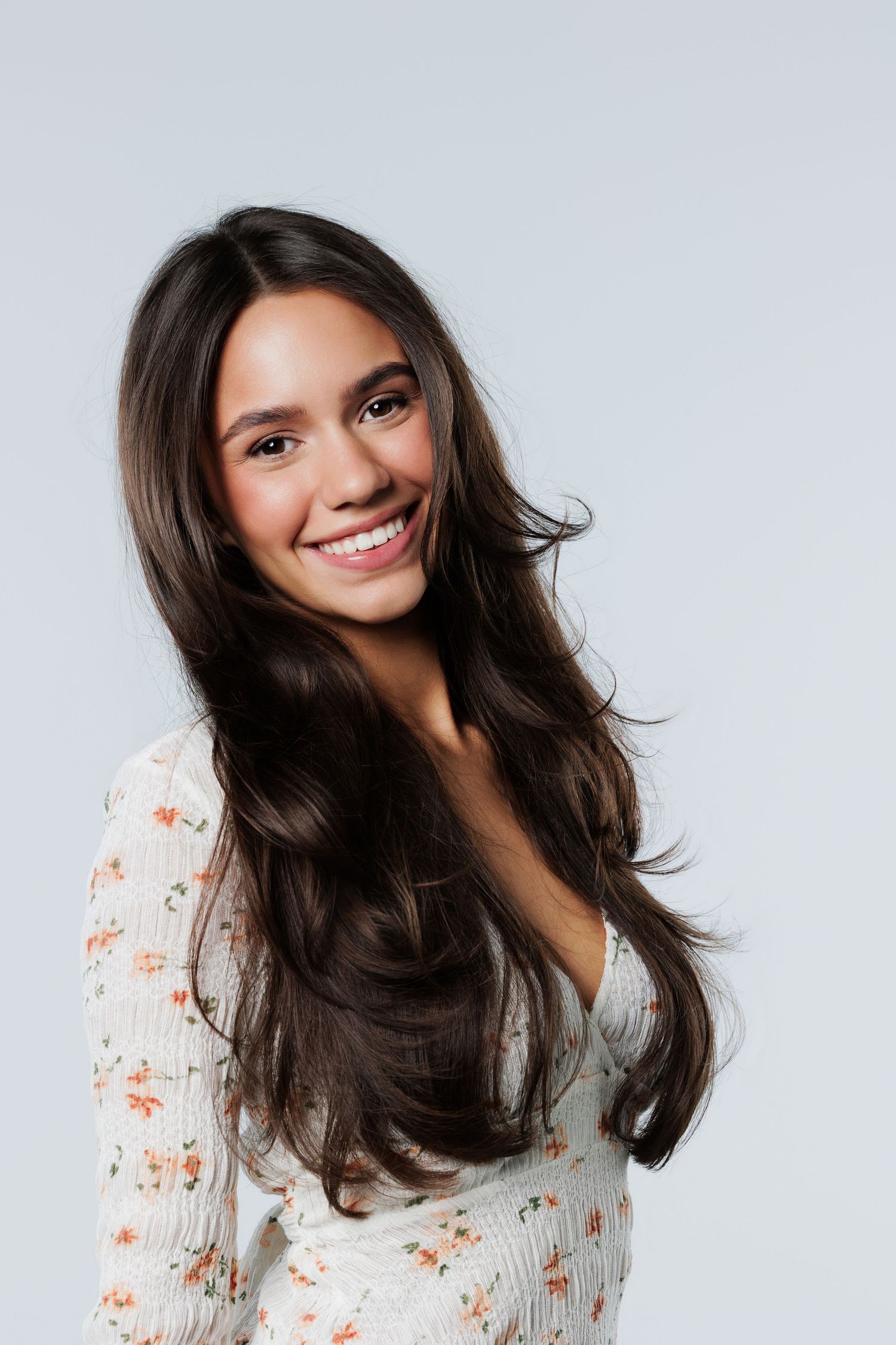 Brunette woman in floral top smiling in studio.