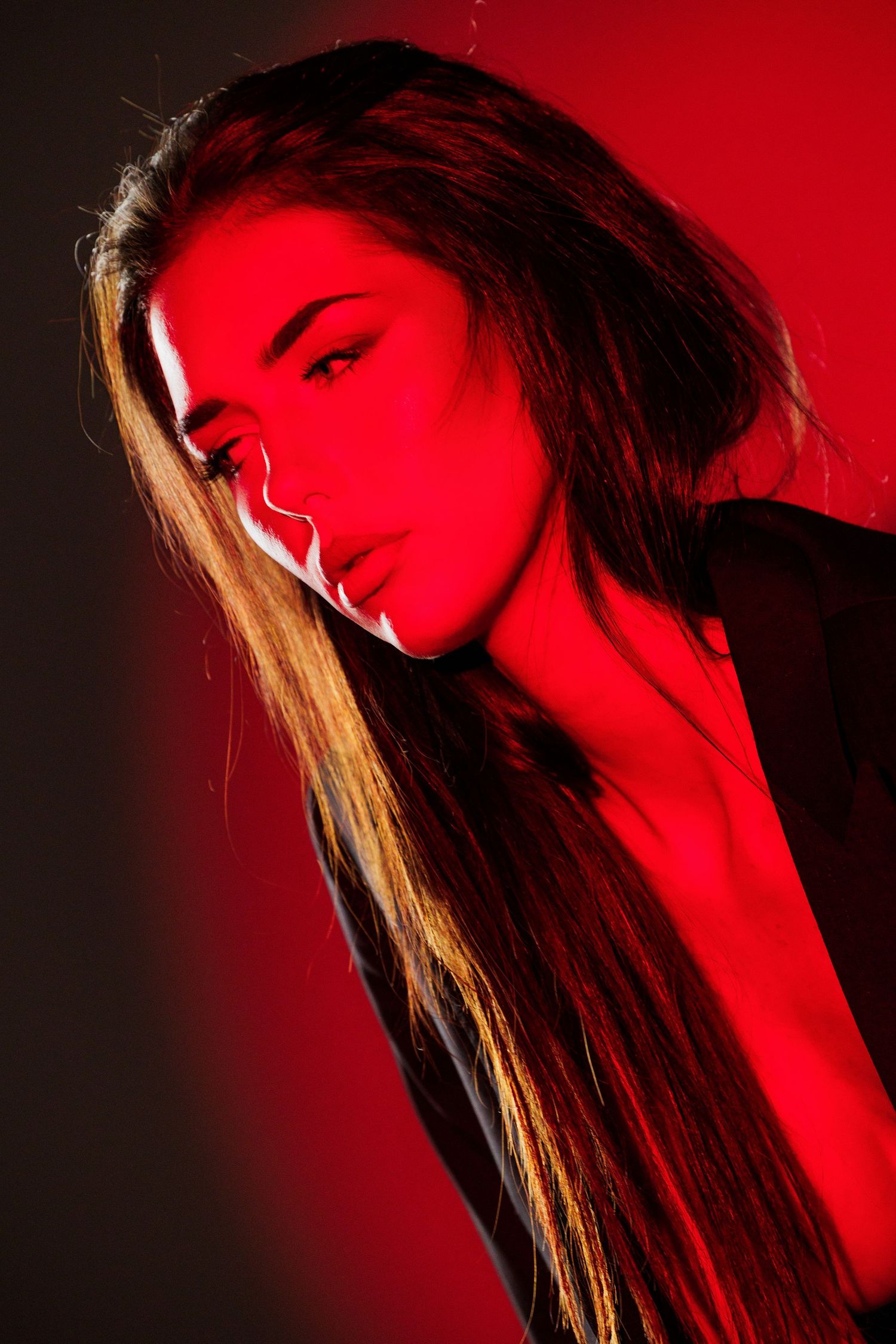 Young woman with long hair posed dramatically under intense red studio lighting against a dark background.