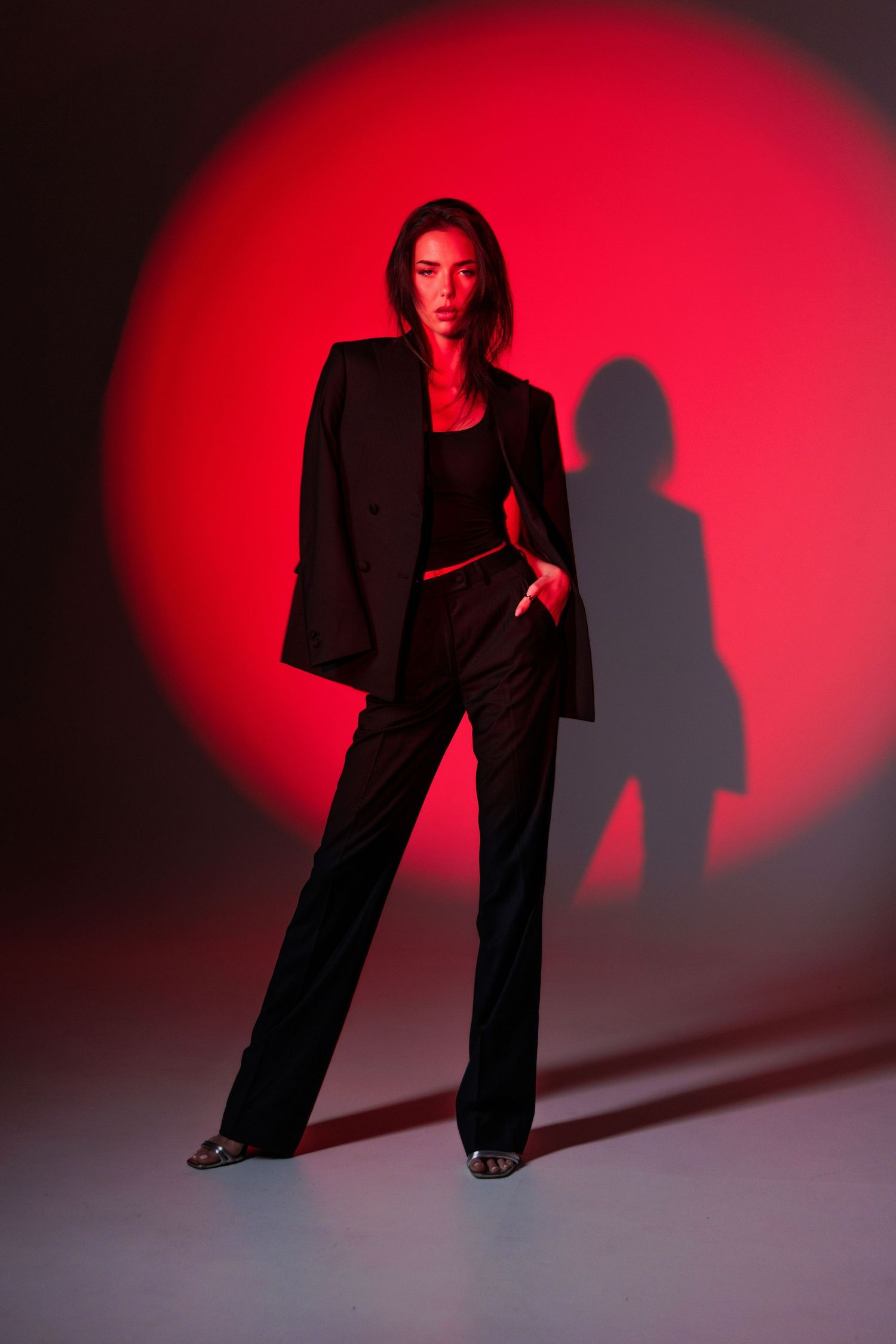 Woman in black oversized blazer and wide-leg trousers posing confidently against a dramatic red spotlight background.